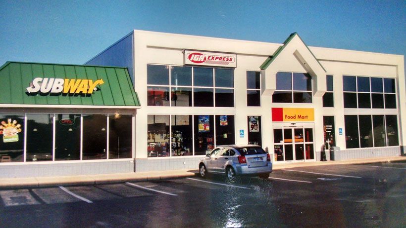 A subway restaurant with a car parked in front of it