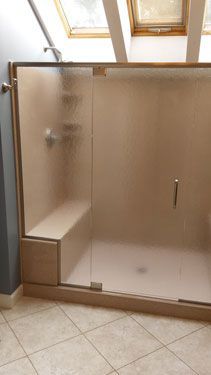 A bathroom with a walk in shower with a bench and a skylight.