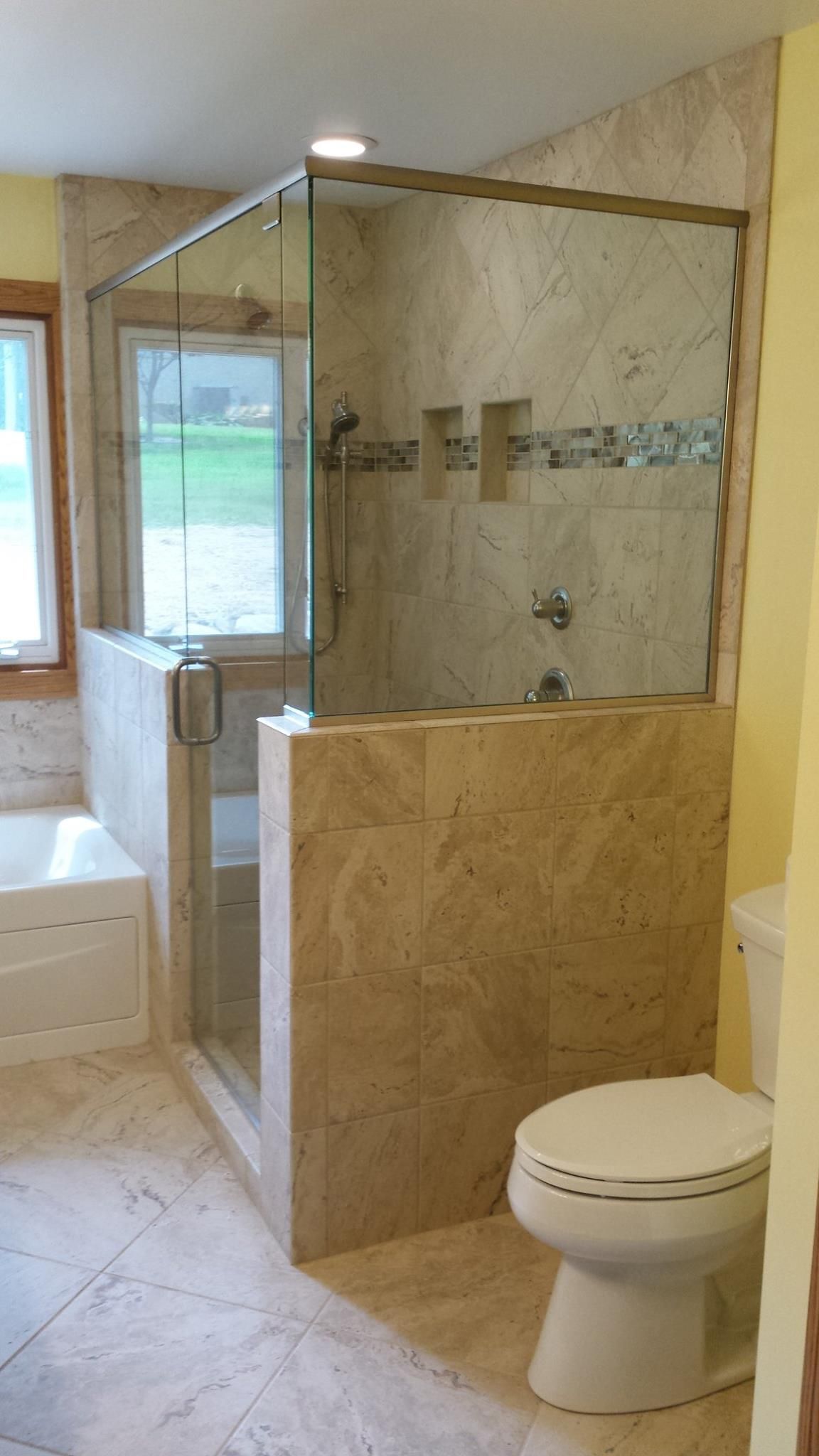 Bathroom with a glass shower enclosure and a toilet. Beige tile is throughout.