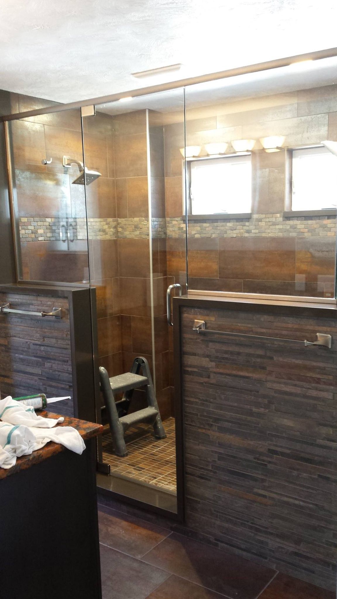 Shower with brown tile walls and glass door, a step stool inside.
