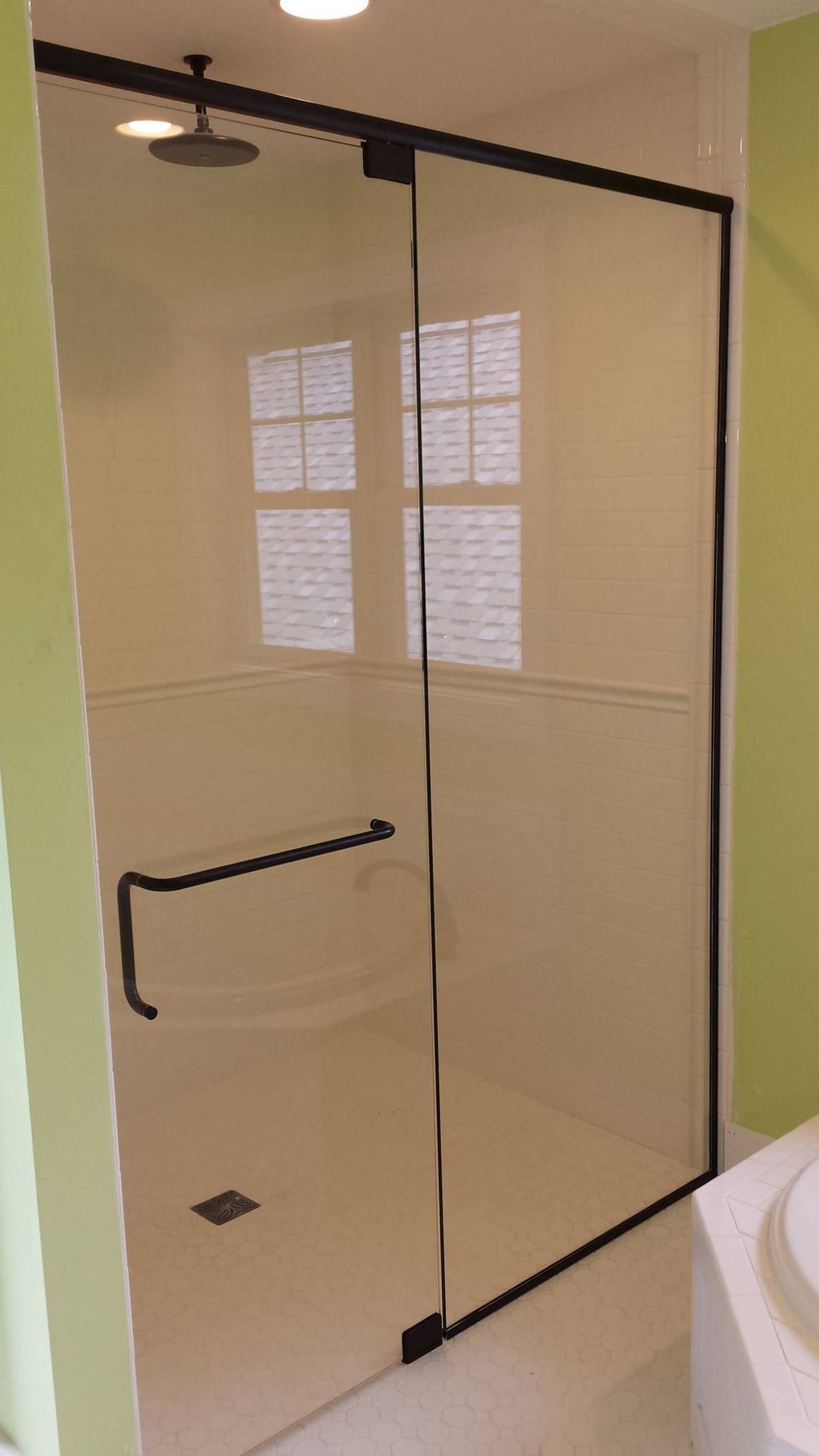 Glass shower with black trim and handle; white interior, window, and light green walls.