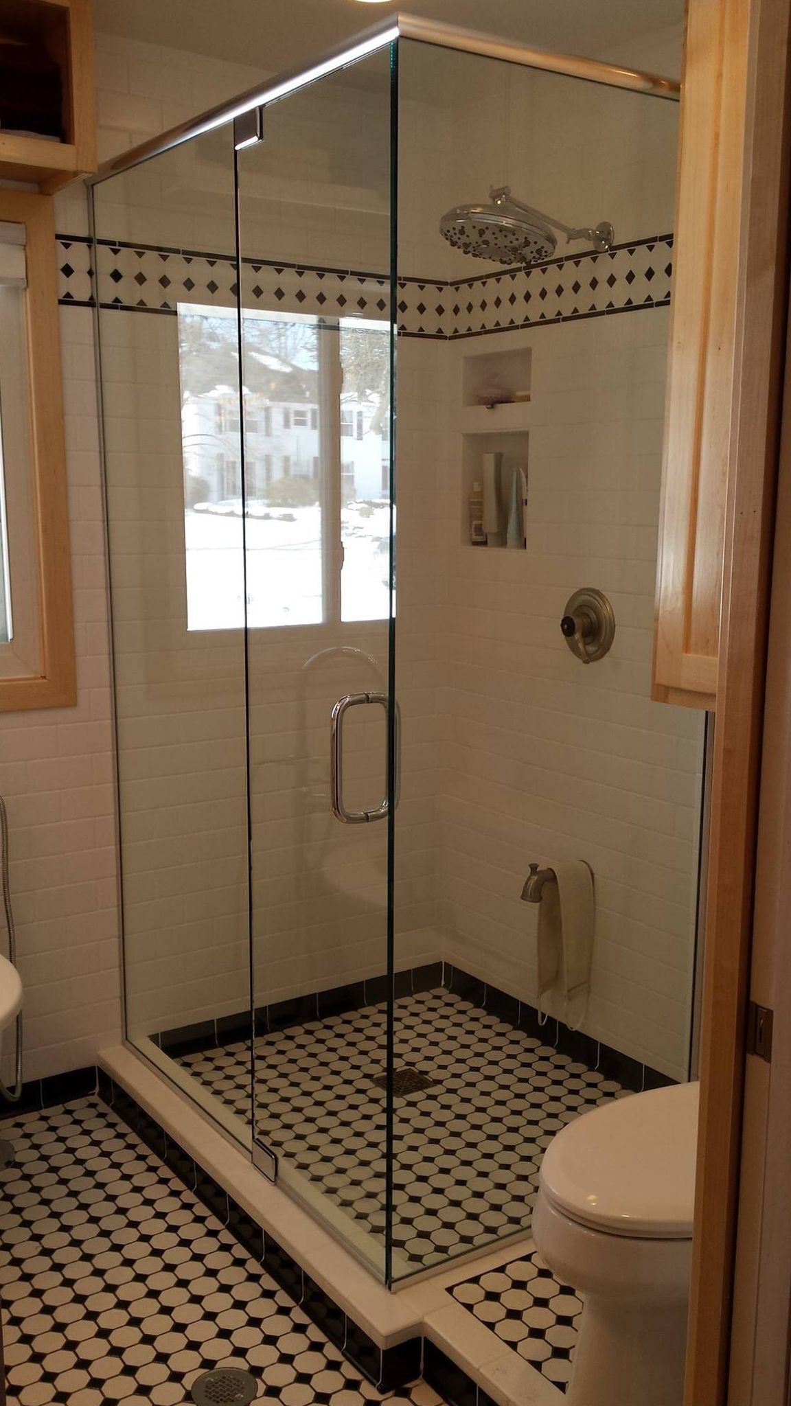 Glass shower in a bathroom with black and white tile flooring.