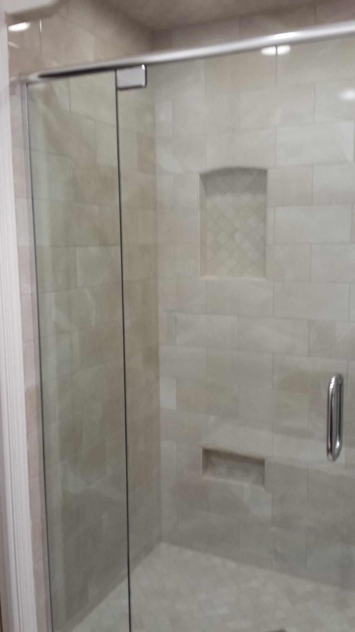 Glass shower enclosure with beige tiled walls, recessed shelf, and handle.