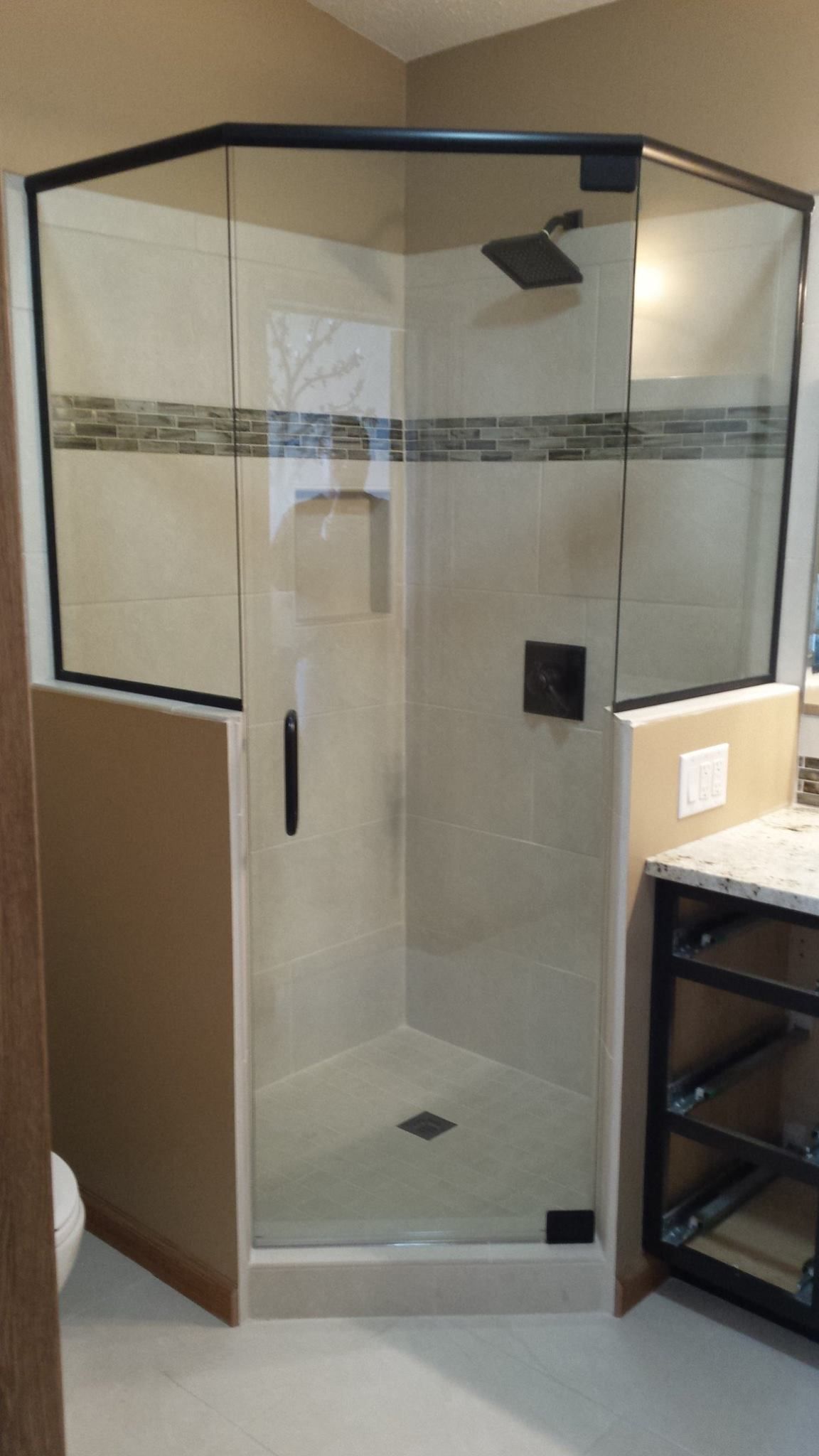 A modern, angled glass shower enclosure with black trim, tile walls, and a shower head.