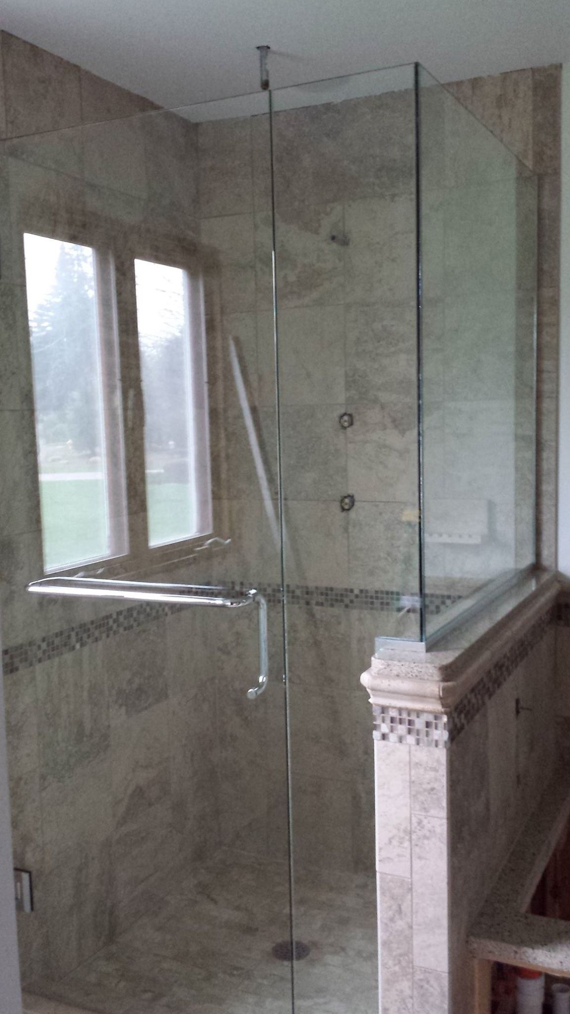 Glass shower enclosure with tiled walls and a window.