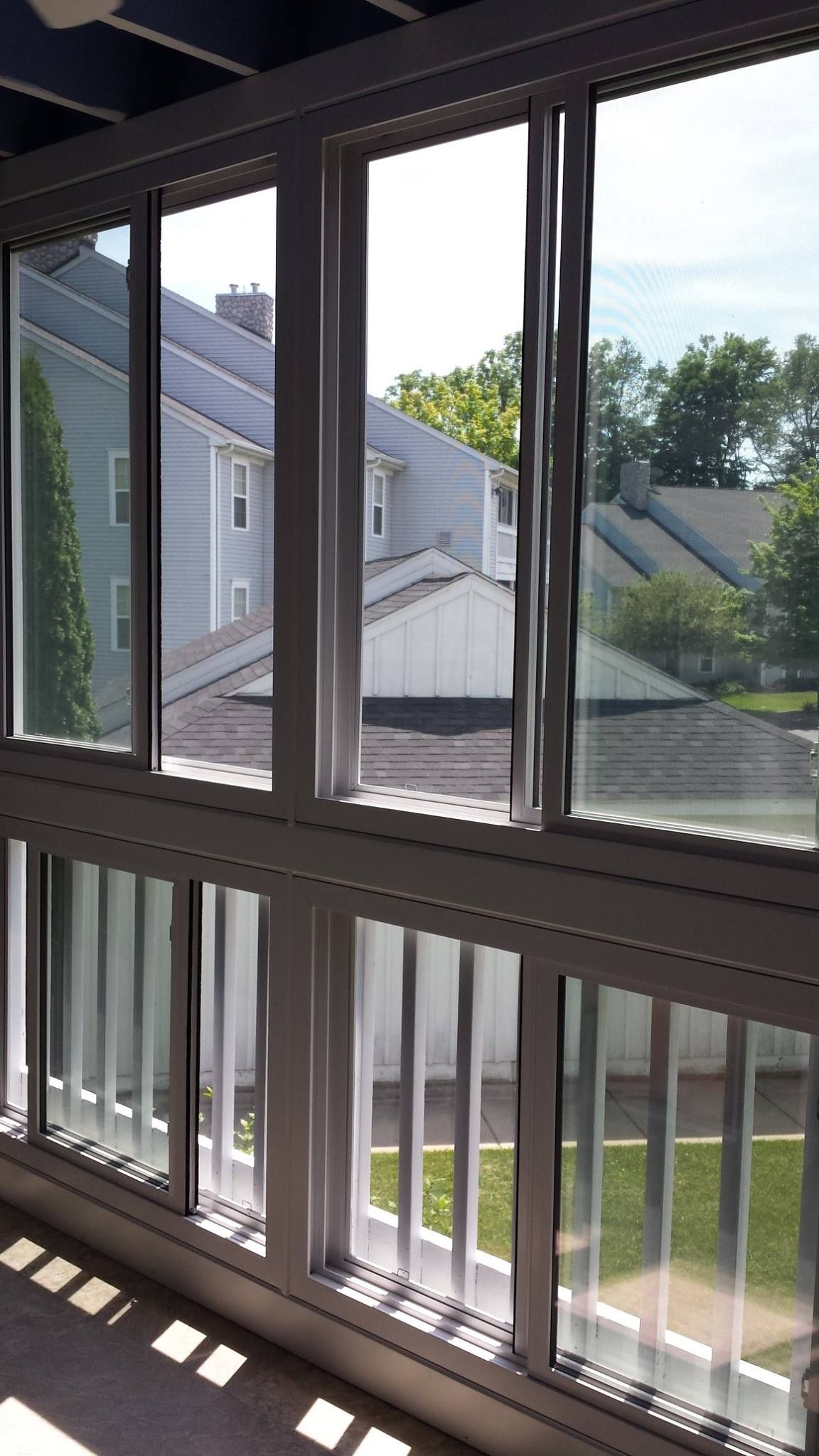 View through a sunroom window; white frame, neighborhood houses, green grass, and bright sunlight.
