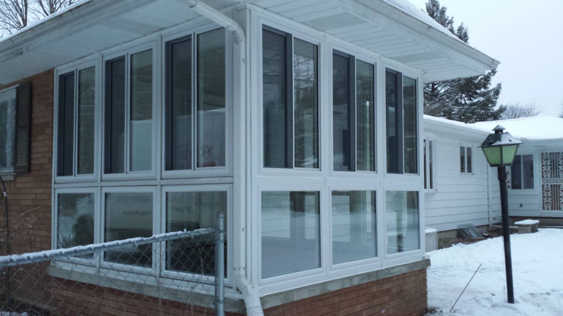 Sunroom addition with many windows on a snowy day. White frames, brick base.