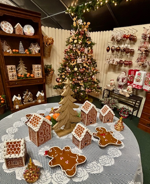 Christmas display: gingerbread houses and tree on a table, ornaments, shelves with holiday decor.