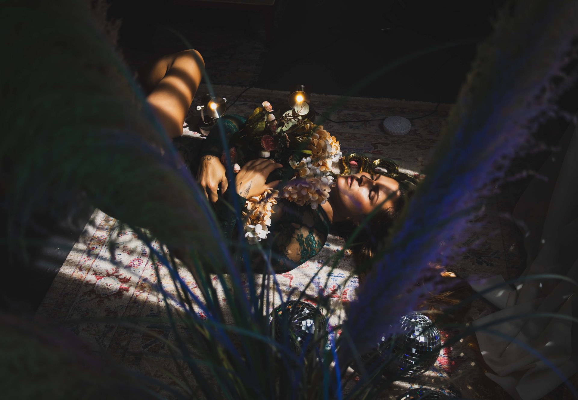 A woman lies surrounded by flowers and candles, lit by a ray of sunlight.