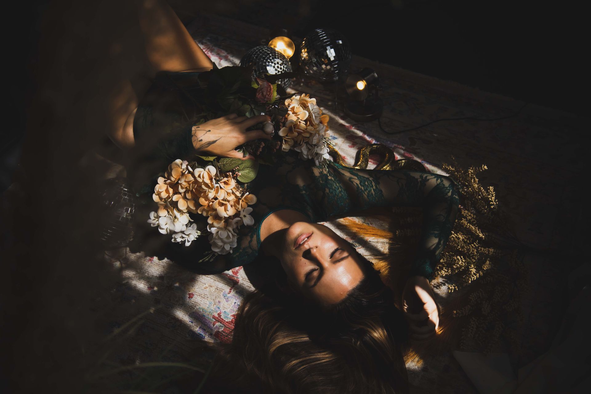 Woman lying on a patterned rug, surrounded by flowers. Warm light bathes her face.