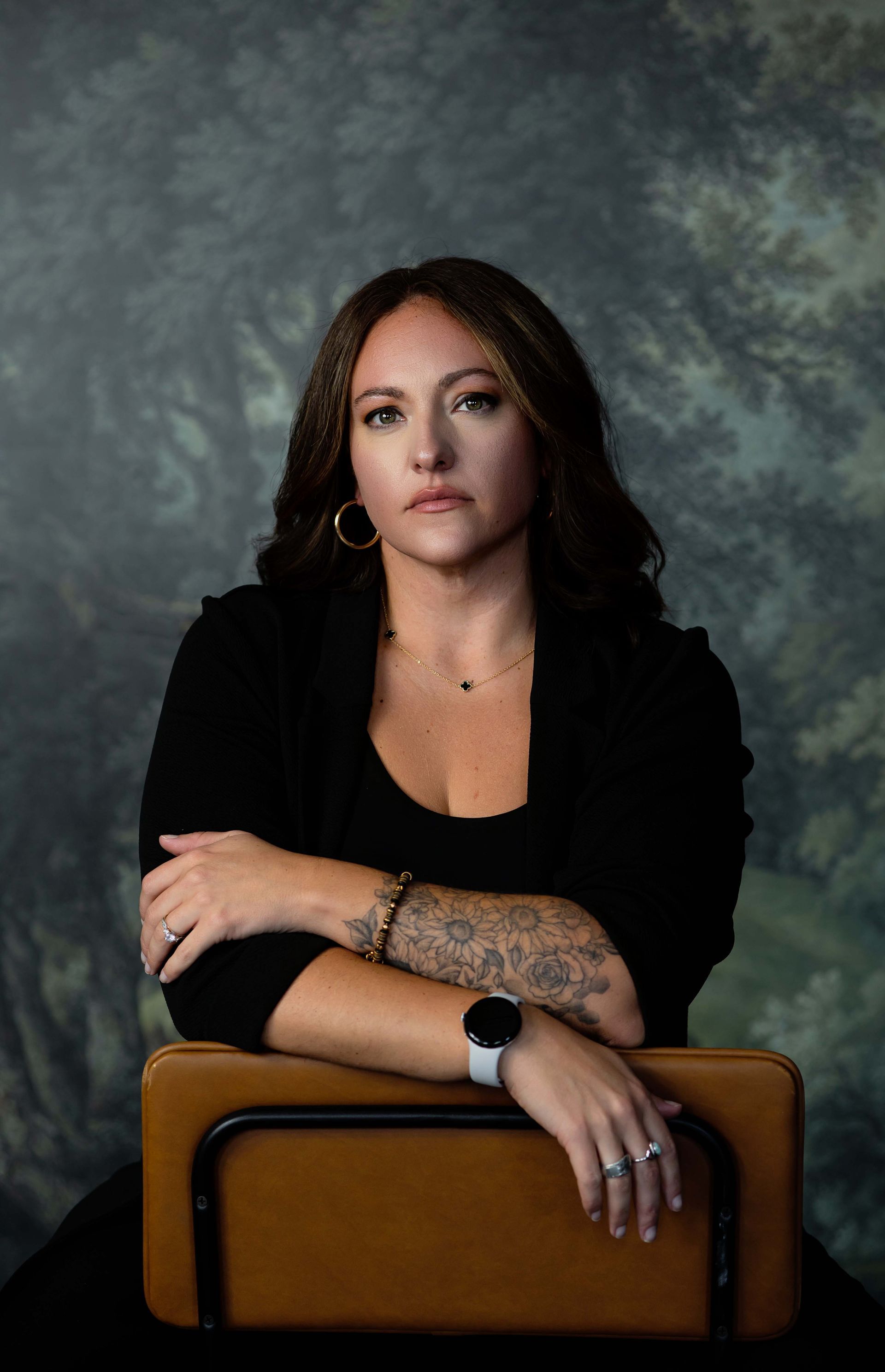 Portrait of a woman with tattoos, leaning on a chair against a gray studio backdrop