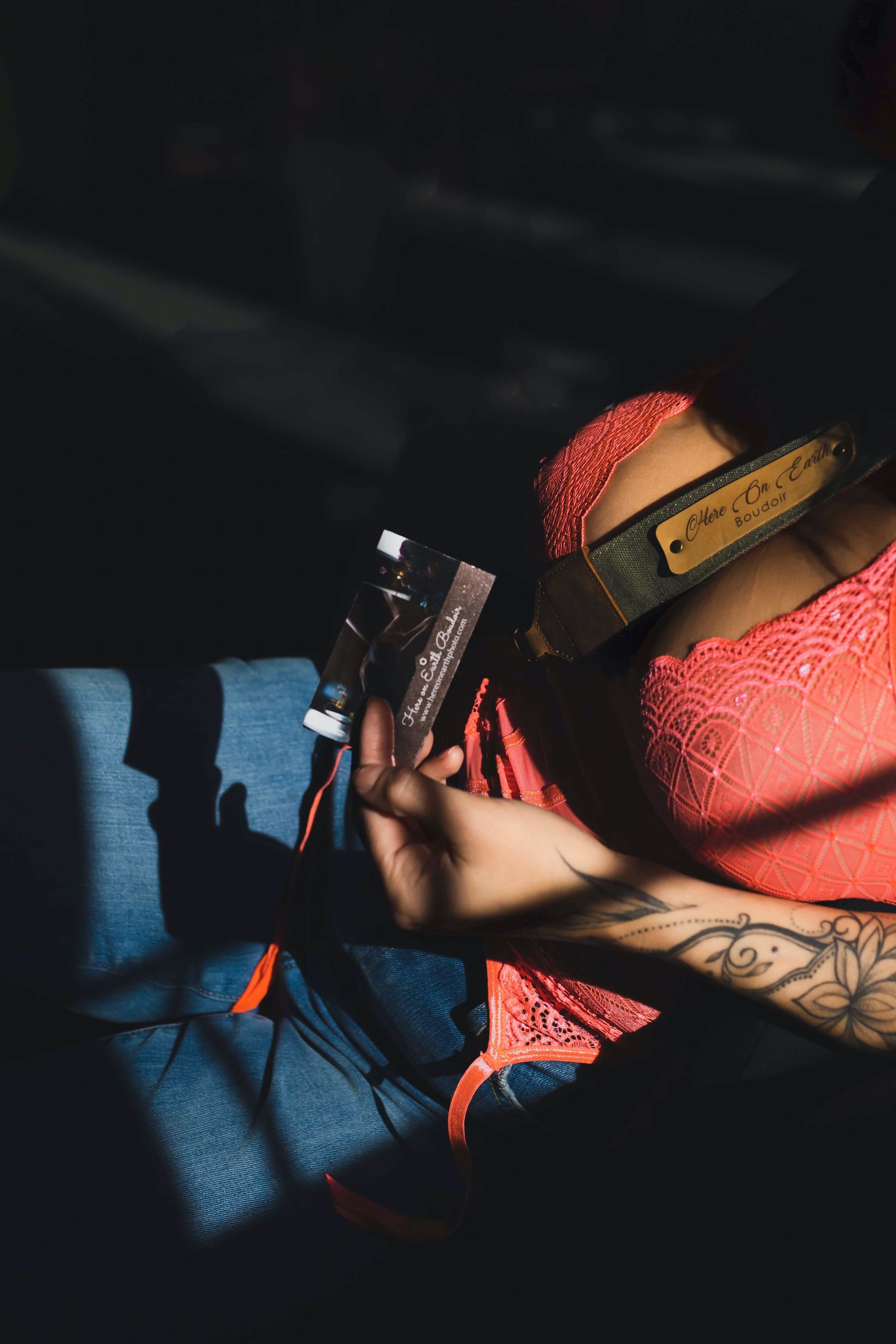 Woman in red lace top sits on blue cushion, holding a package. Arm tattoo visible.