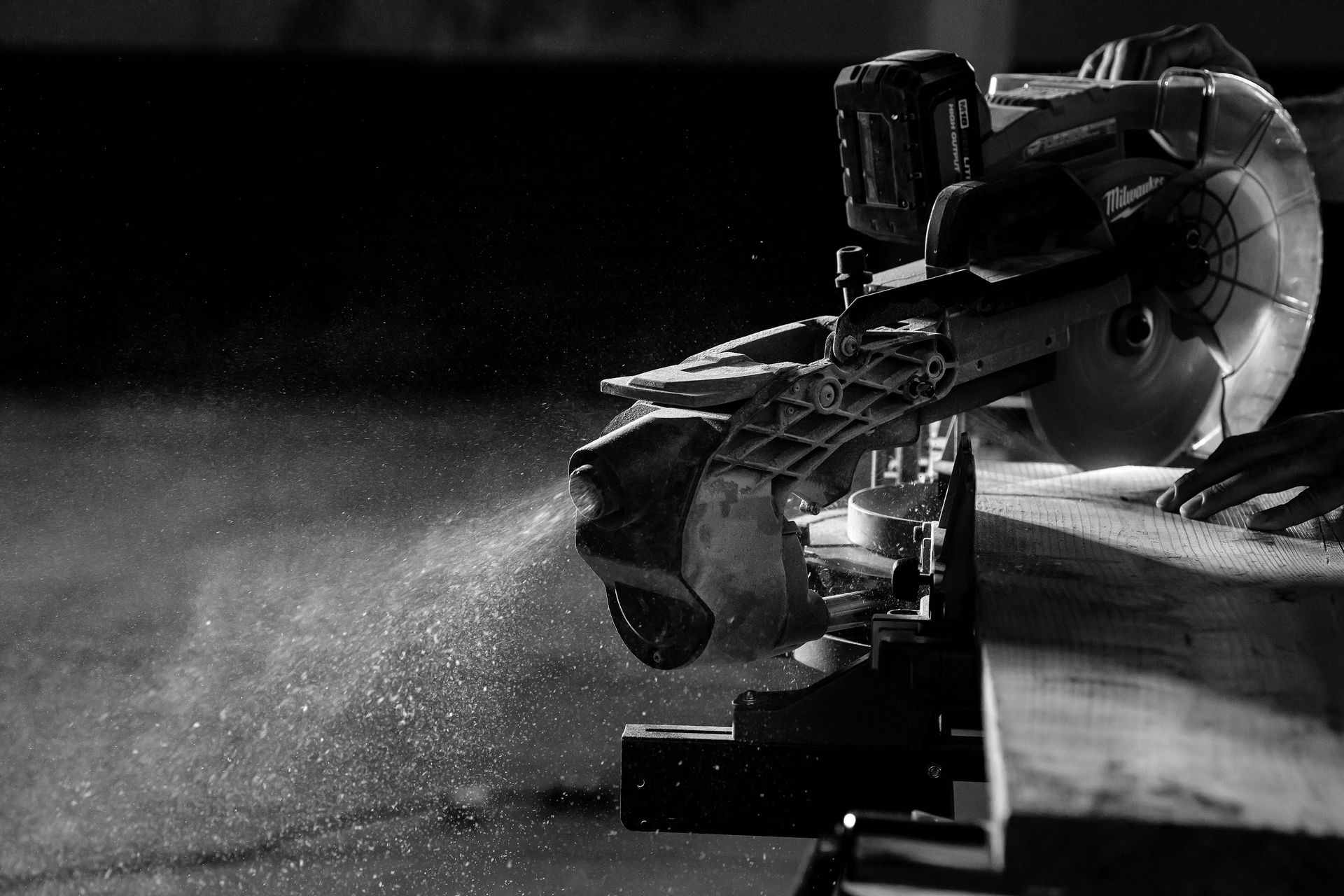 Miter saw cutting wood, releasing sawdust. Close up shot in black and white.