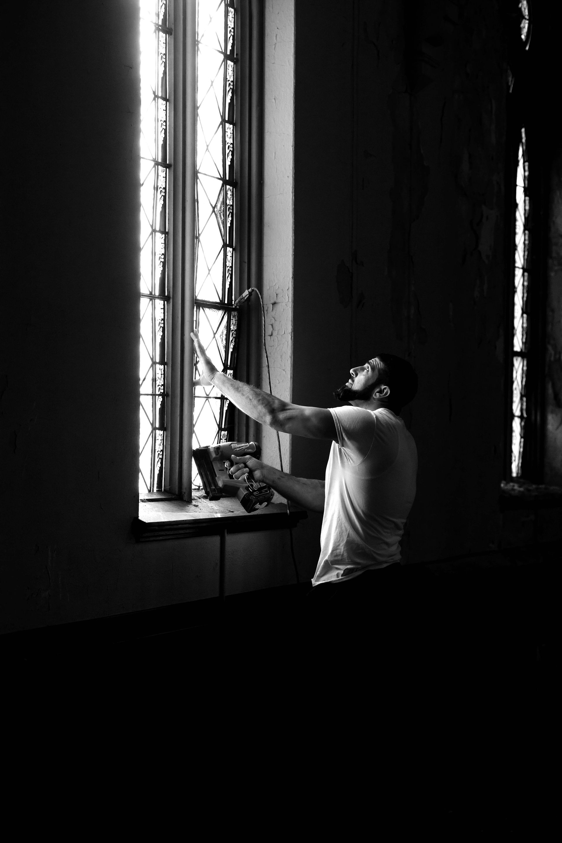 Man reaching towards light streaming through a tall window in a dark room.