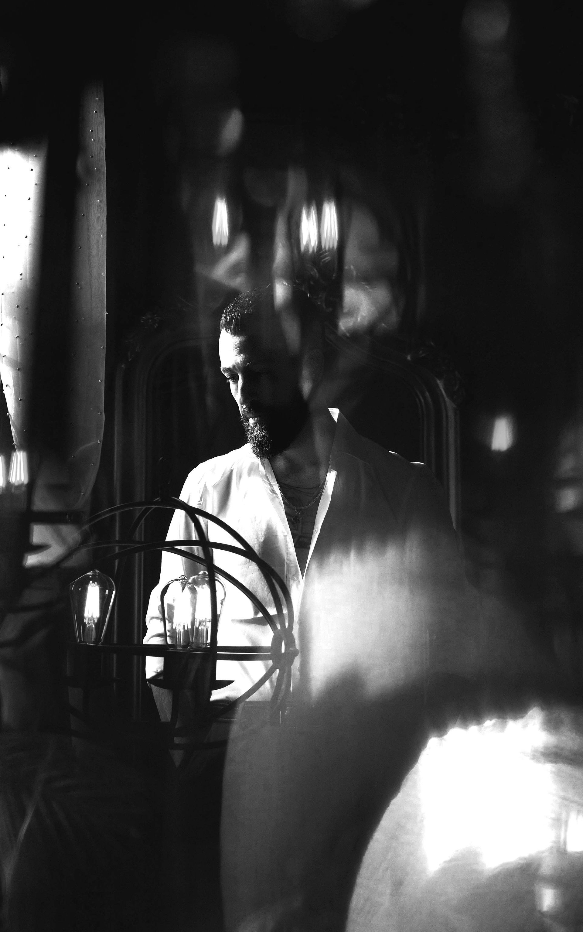 Man standing inside a room with blurred lights, wearing a white shirt, with a serious expression.