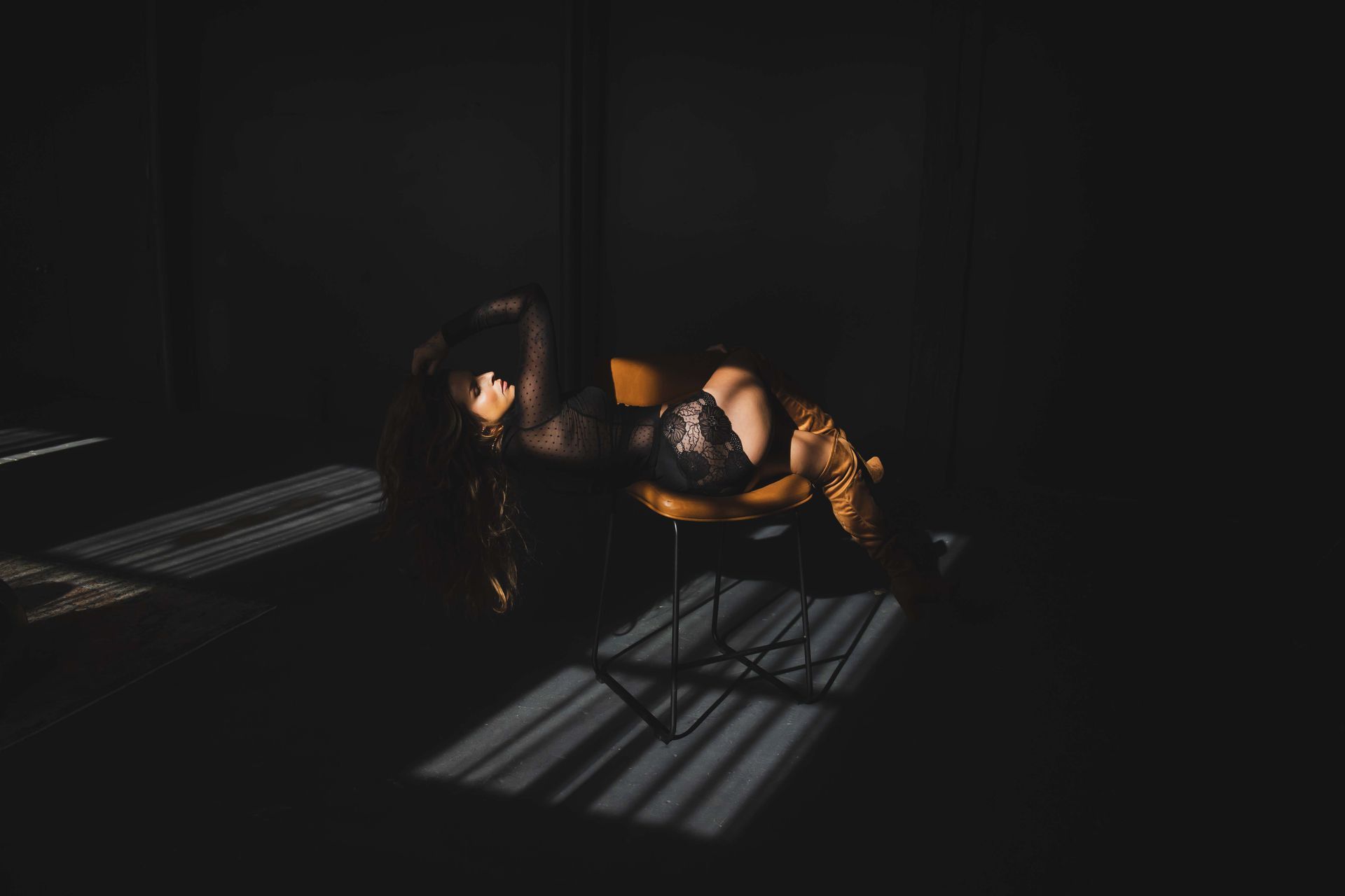 A woman reclines on a chair, draped in shadows with sunlight across the floor.