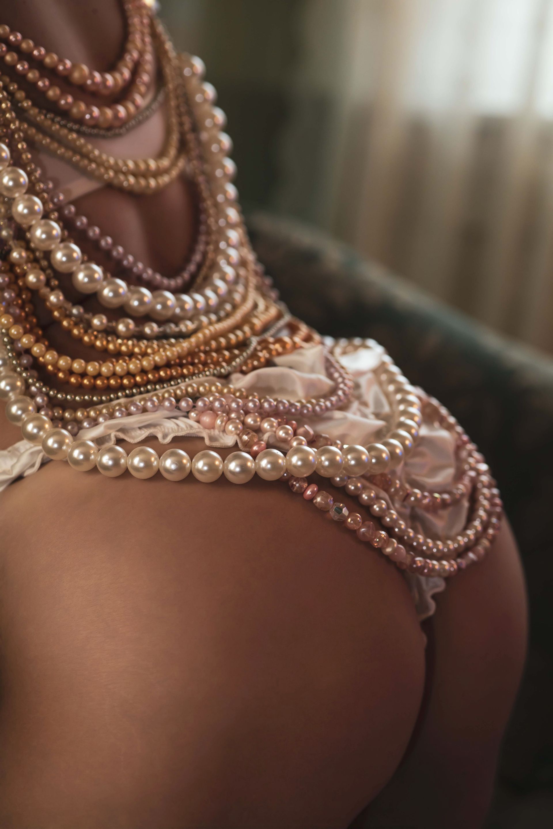 A person's back and buttocks adorned with numerous strands of pearls and a lacy, pearl-embellished underwear.