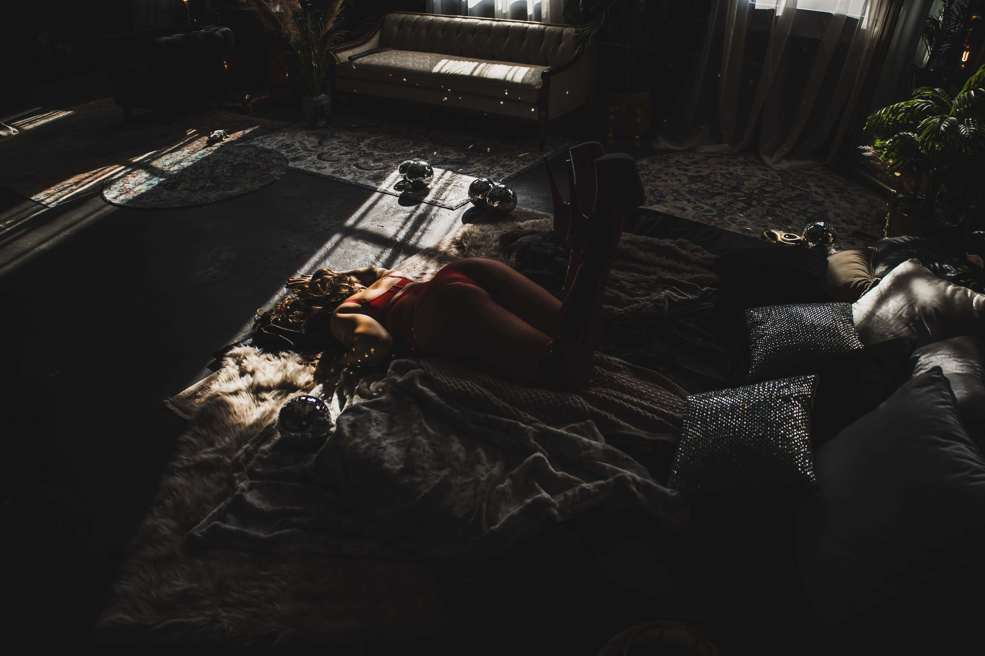 A woman lies on a rug in a dimly lit room. Sunlight streams in, illuminating her and the surrounding decor.