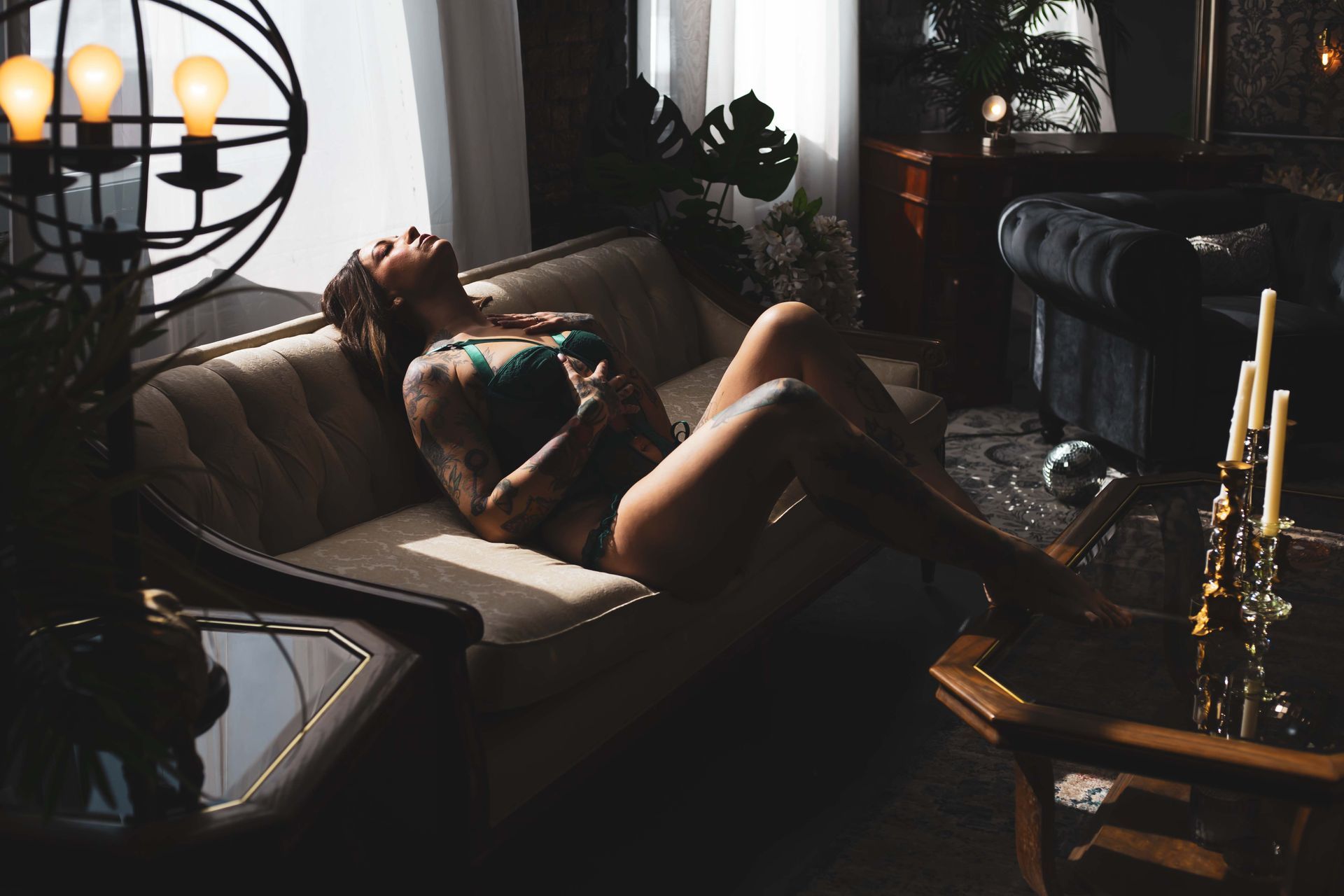 Woman reclines on a cream sofa, bathed in sunlight, arms raised, surrounded by vintage decor.