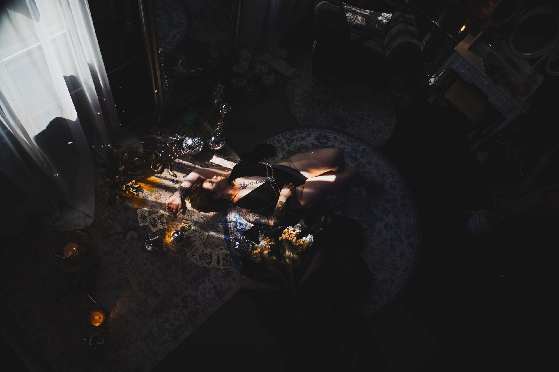 Bright sunlight streams onto a dimly lit room with a table, flowers, and a person sleeping on a patterned comforter.