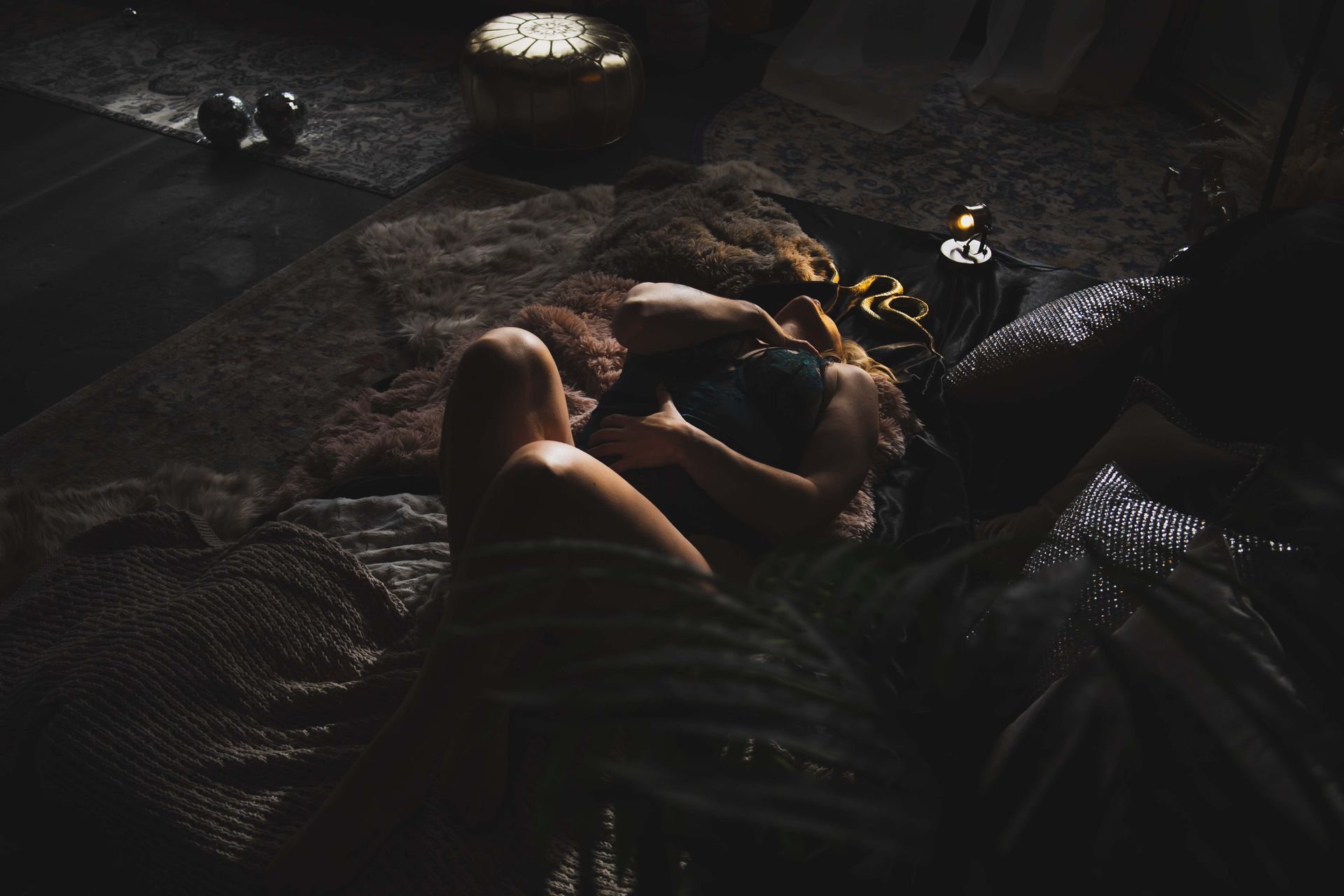 Two people embraced on a bed, partially covered by blankets in a dim room. Soft light falls across them and the textured bedding.