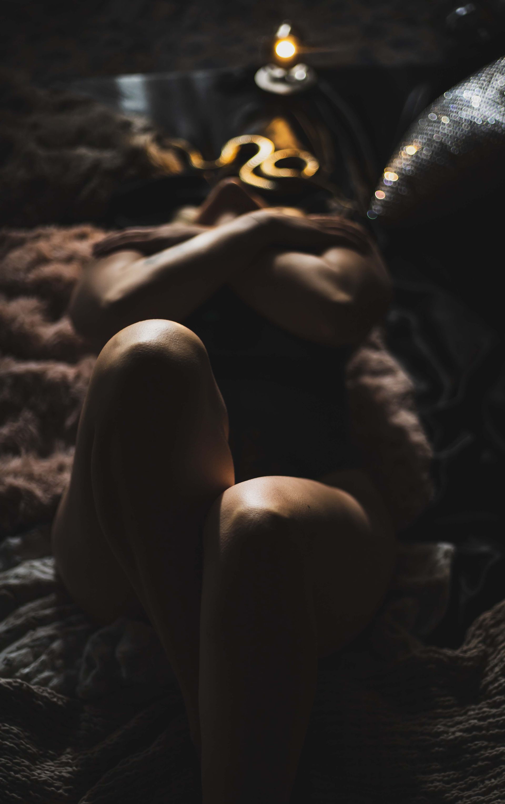 Person lying on a fluffy surface, arms crossed. Knees bent, legs up. Soft lighting, dark colors.
