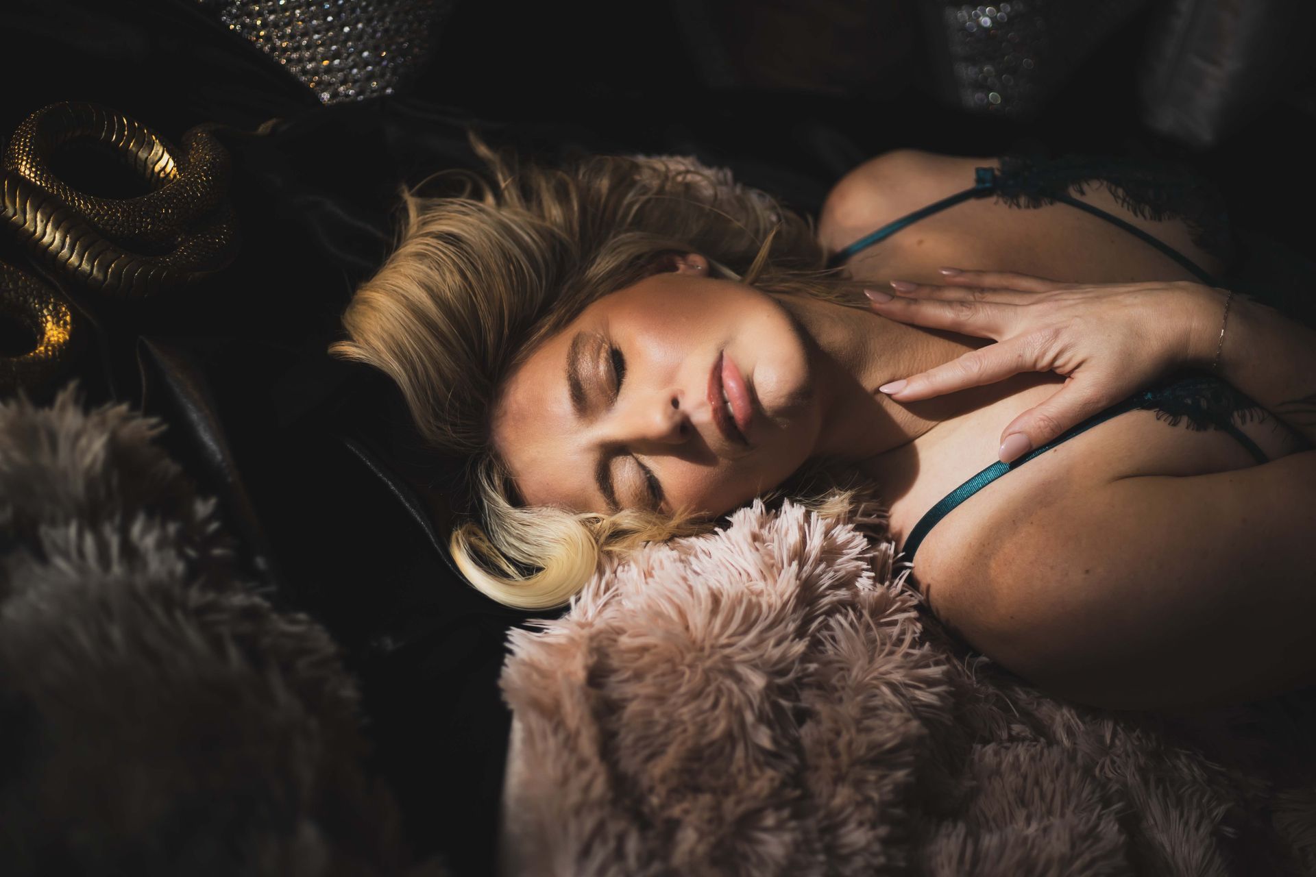 Blonde woman in teal lingerie asleep on a fluffy pink blanket, resting her hand on her chest.