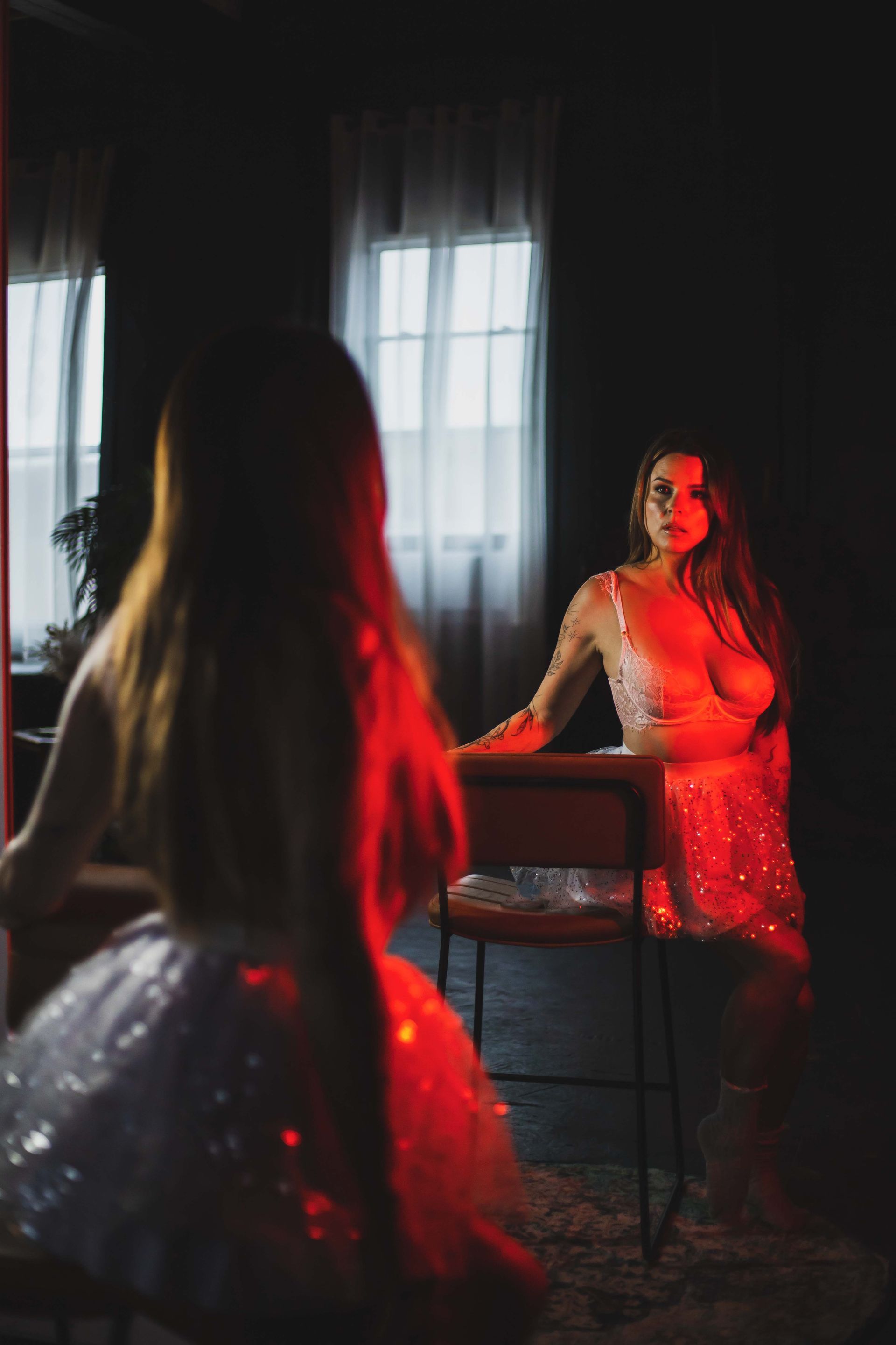 Woman in a sparkly dress looks in a mirror. Red light illuminates her and the room.