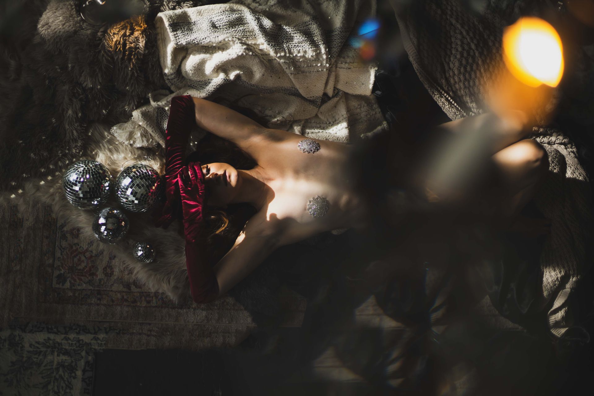 A person lies amongst disco balls and a net. Light reflects off their chest, casting shadows.