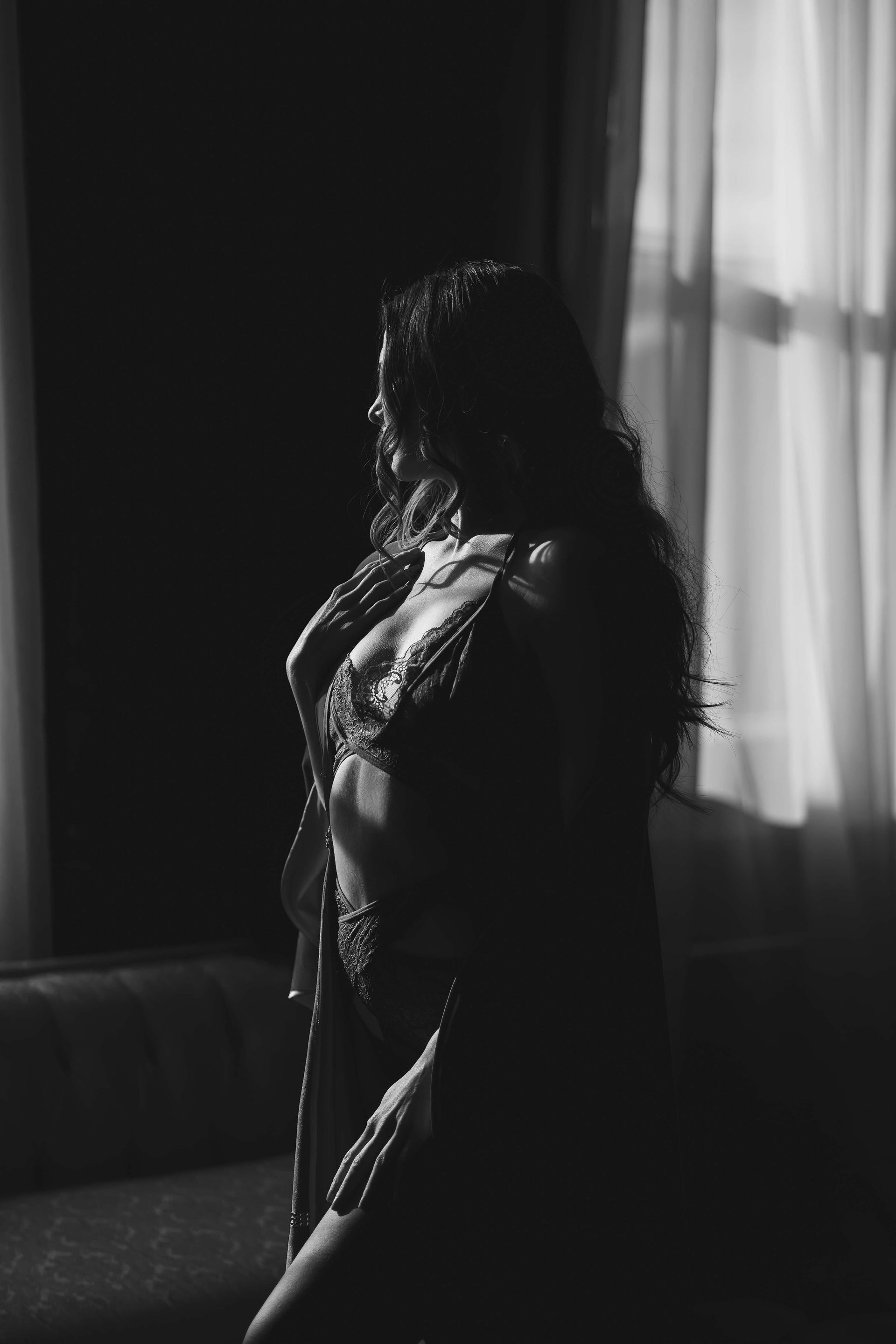 Woman in lingerie, silhouetted against a sunlit window, posing in an interior setting.