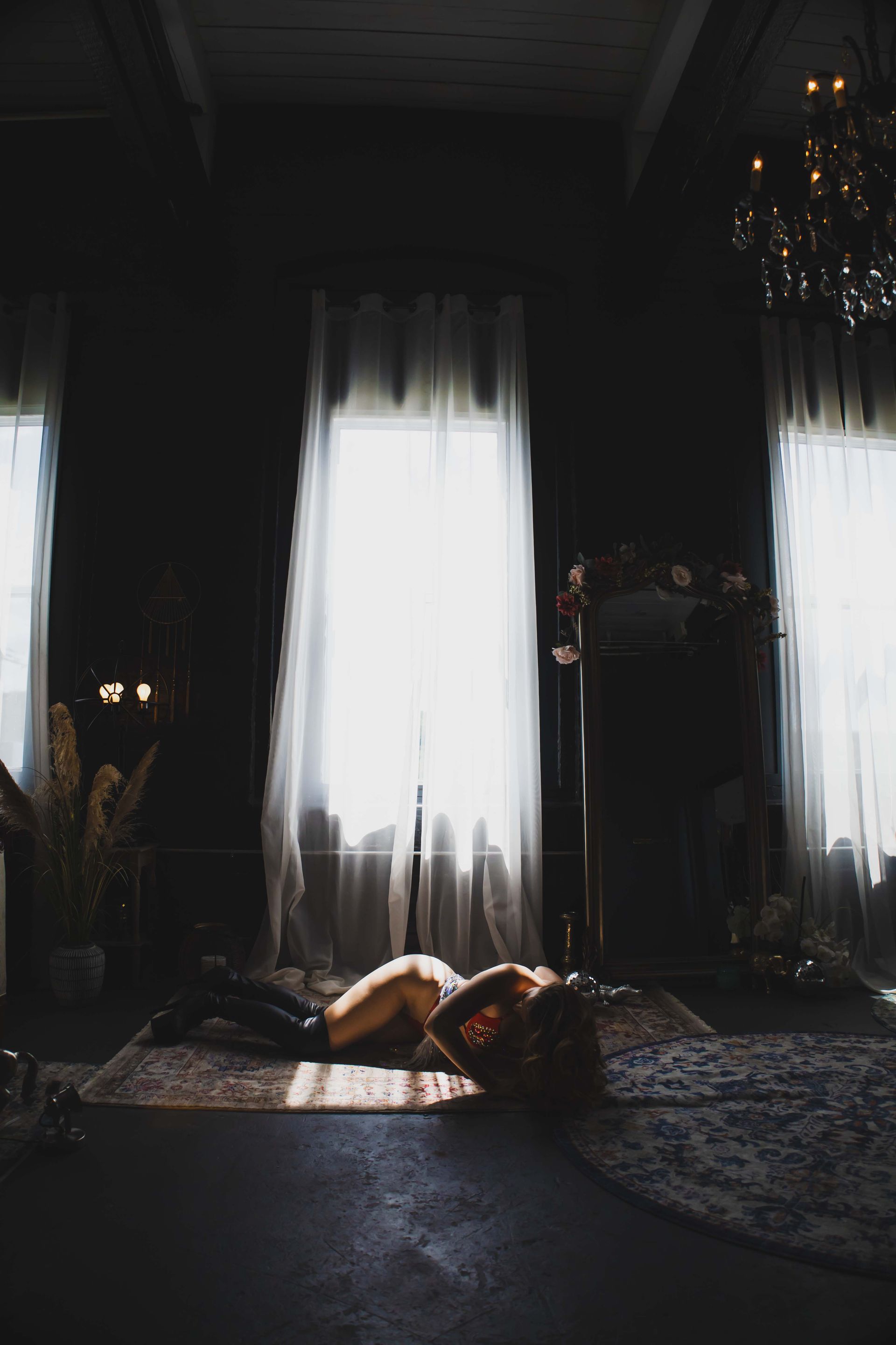 Woman reclining on a rug in a dark room, bathed in light from a large window.