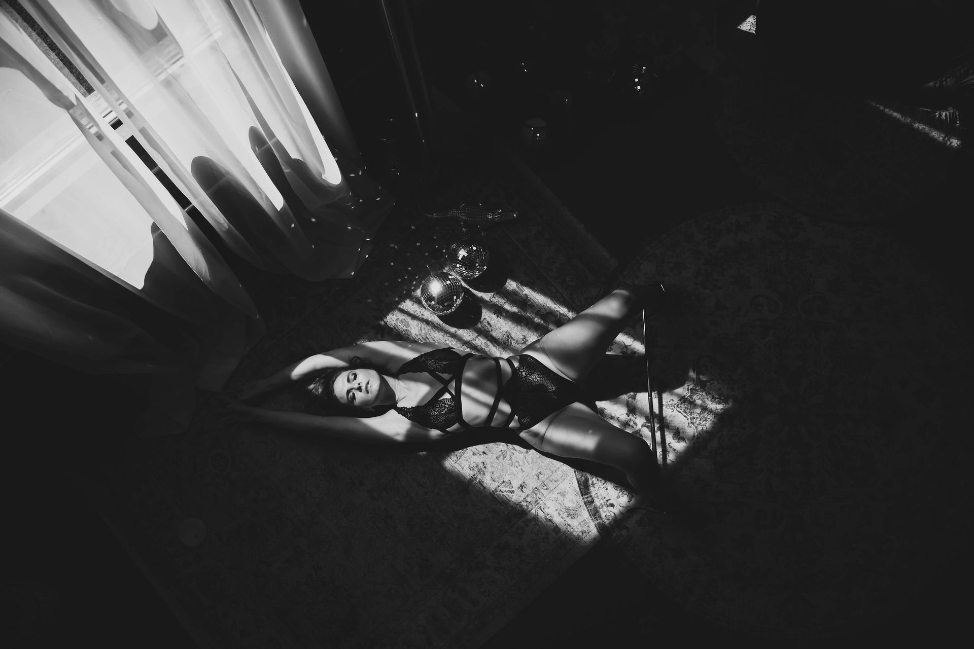 A woman reclines on a rug, lit by sunlight streaming through a window. Black and white, she gazes upward, appearing relaxed.