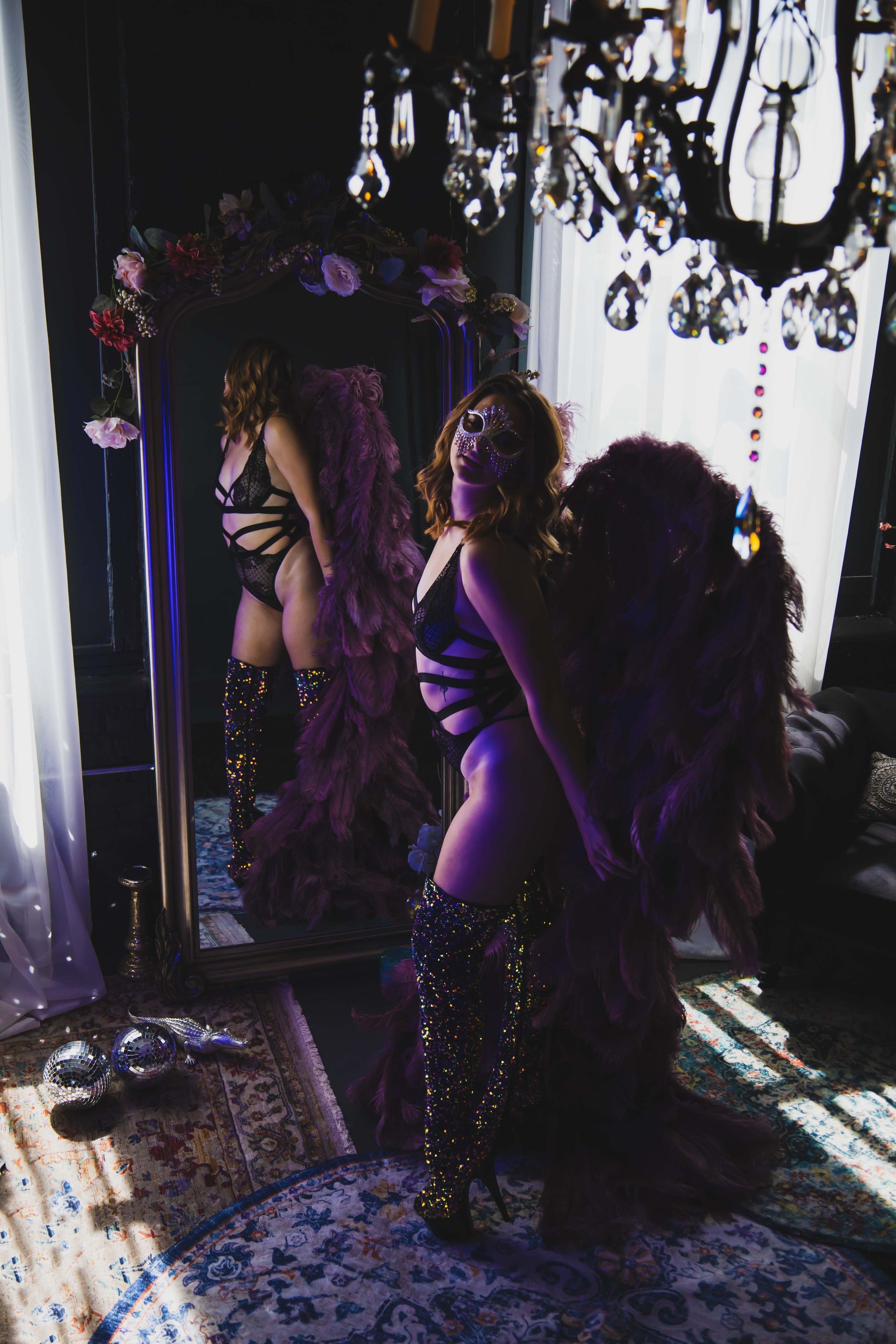 Woman in lingerie and feathered wings poses in front of a mirror. She is wearing sparkly boots.
