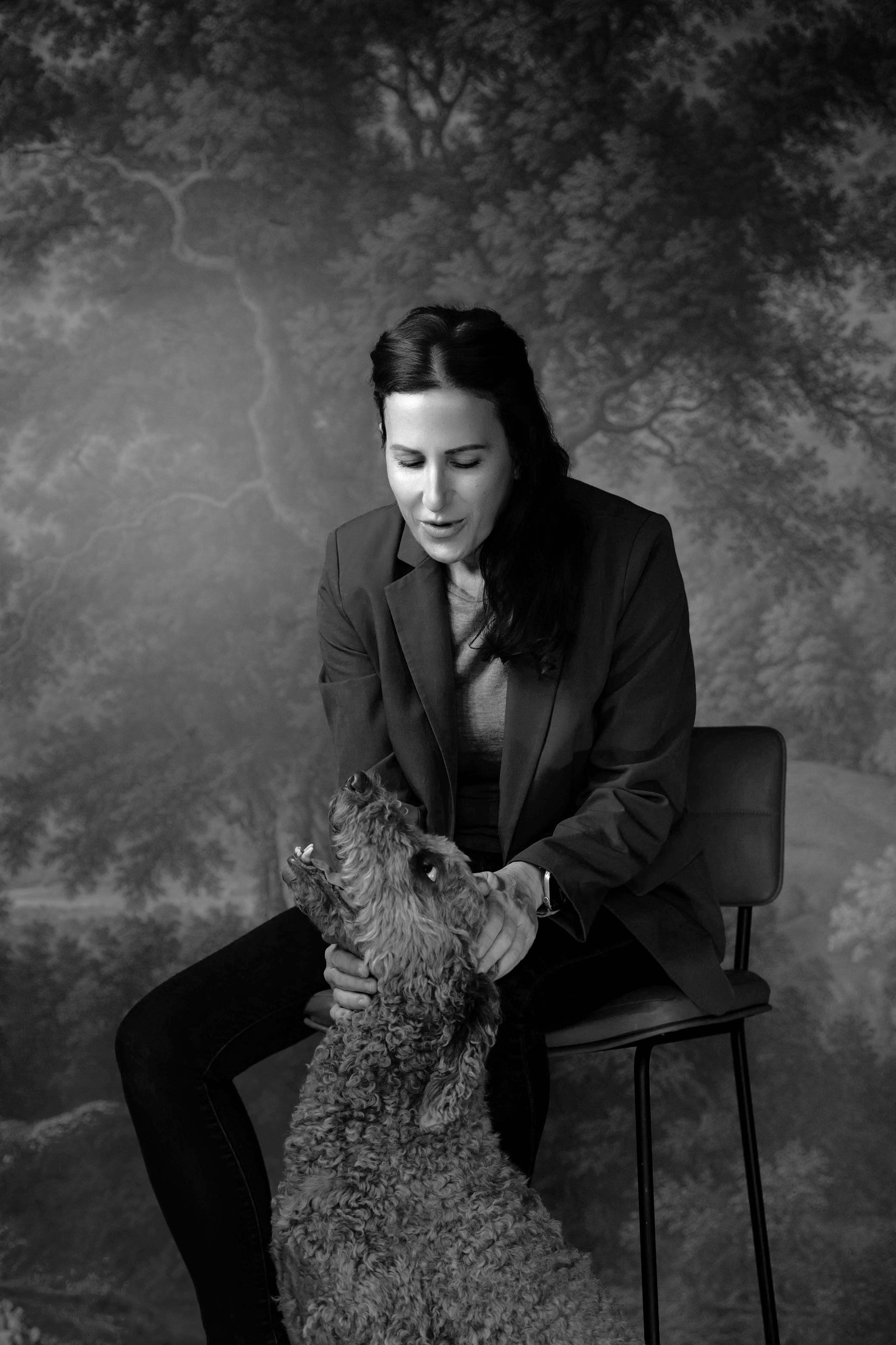 Seated person in a dark suit holding a patterned scarf against a textured studio backdrop