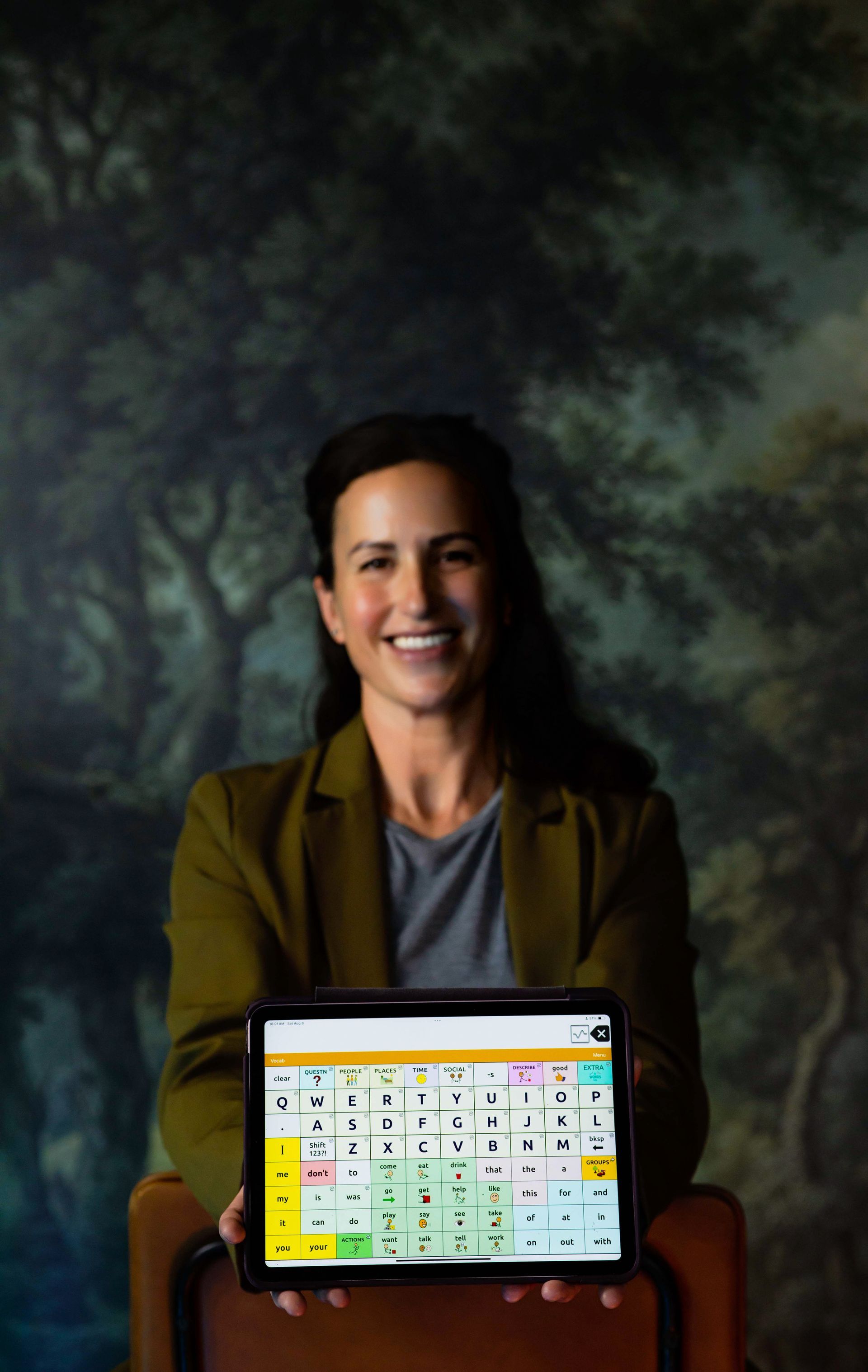 Smiling person holding a tablet with a map on screen against a dark background