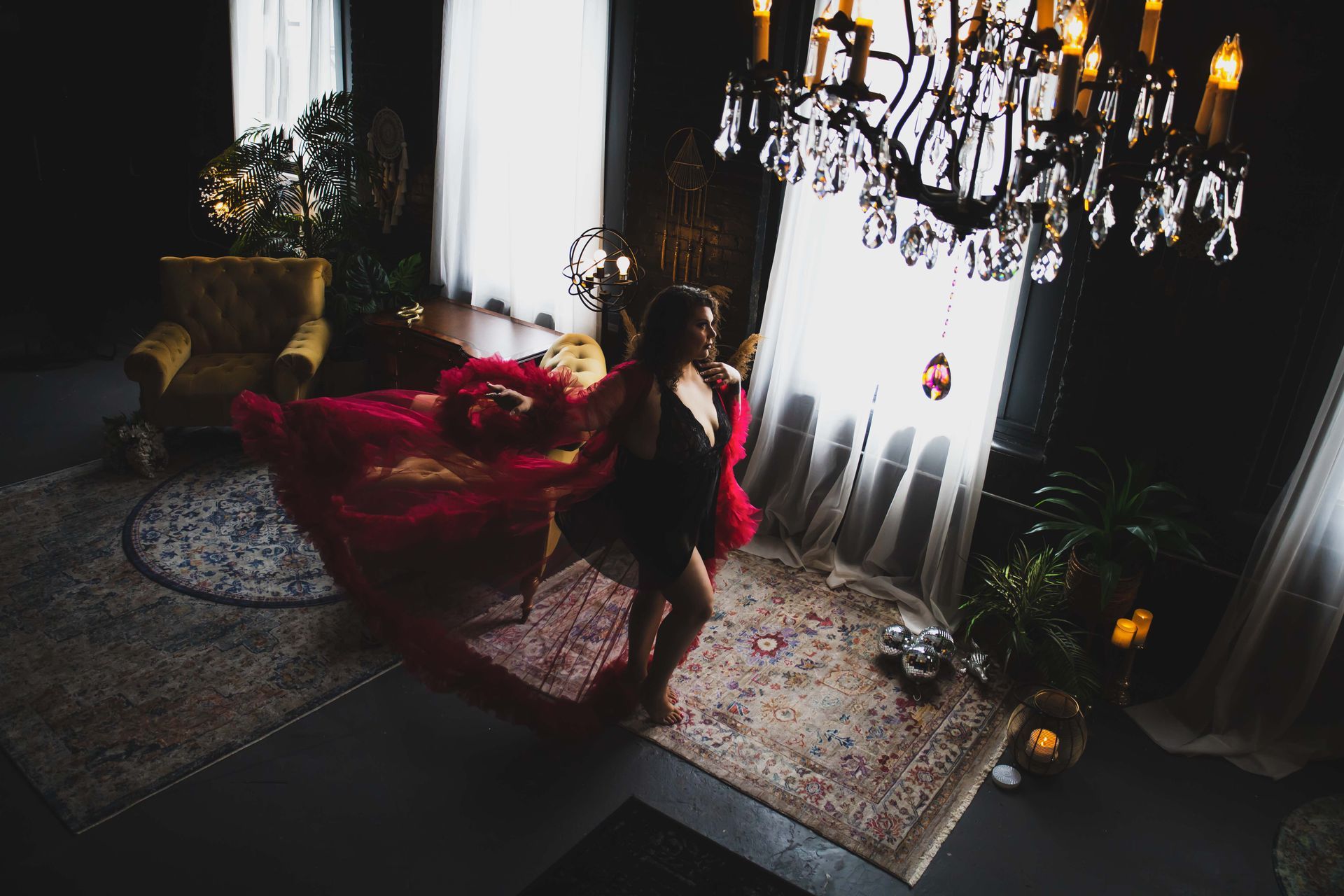 Woman in lingerie dances in a dark room with a crystal chandelier, rugs, and a gold chair.