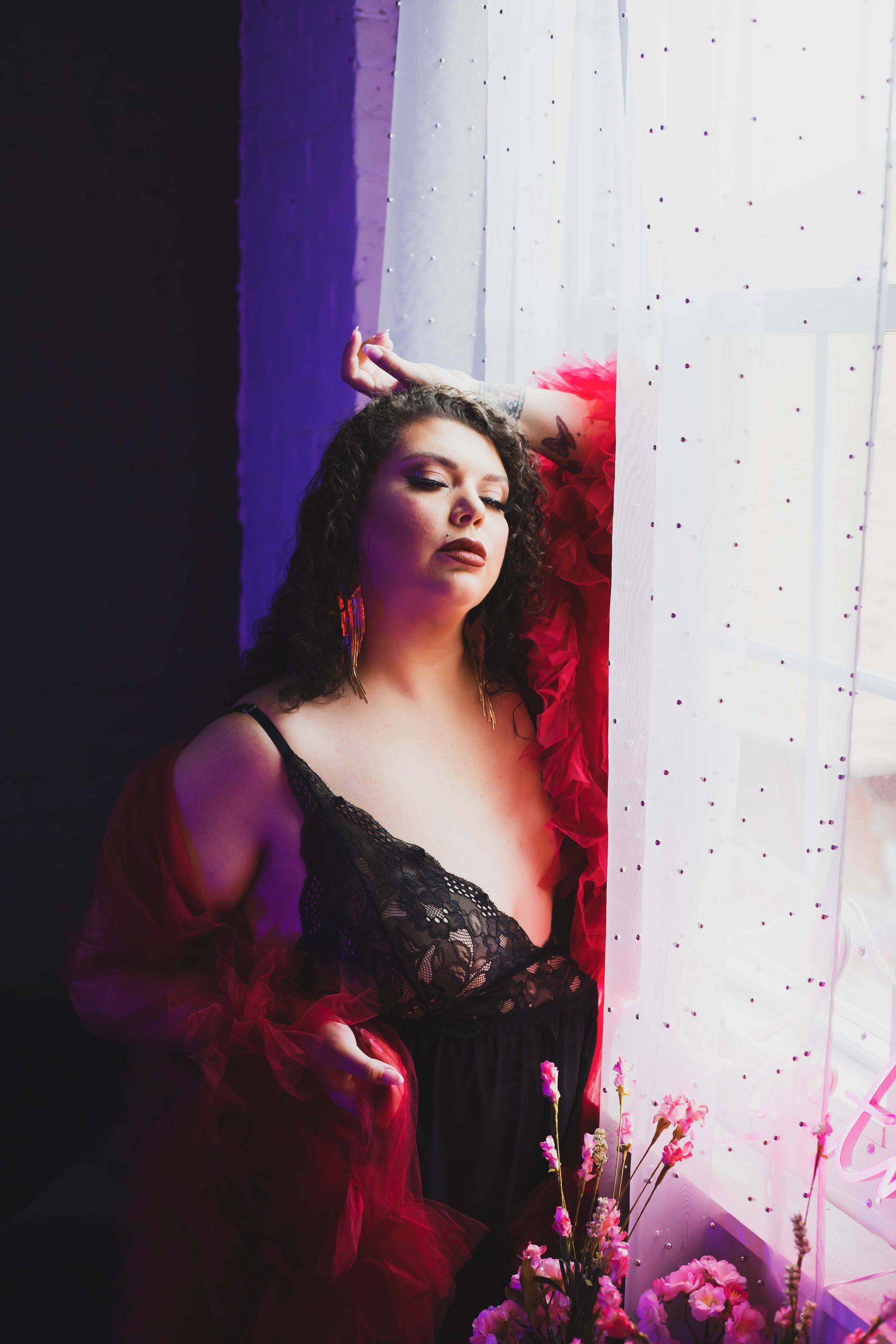 Woman in black lingerie leans against a window, hand on head, red boa draped around her. Purple and pink lighting.