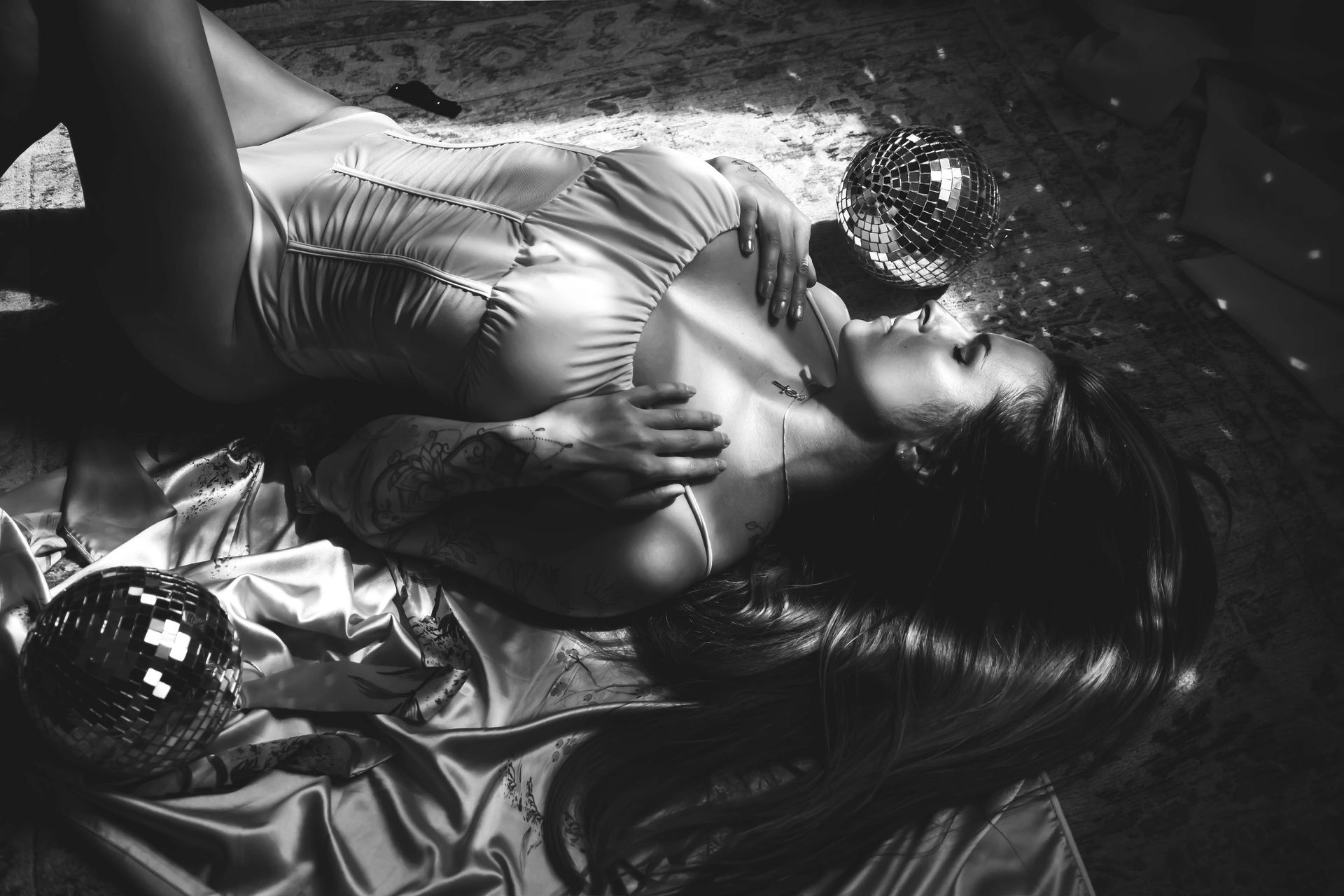 Woman reclining on satin, illuminated by disco balls. Black and white photo.