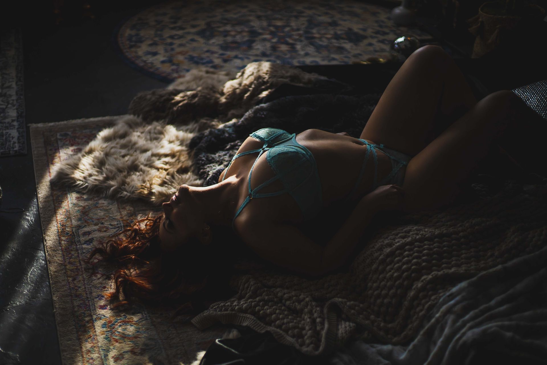 Woman in light blue lingerie reclines on a bed with fur and knitted blankets, bathed in sunlight.