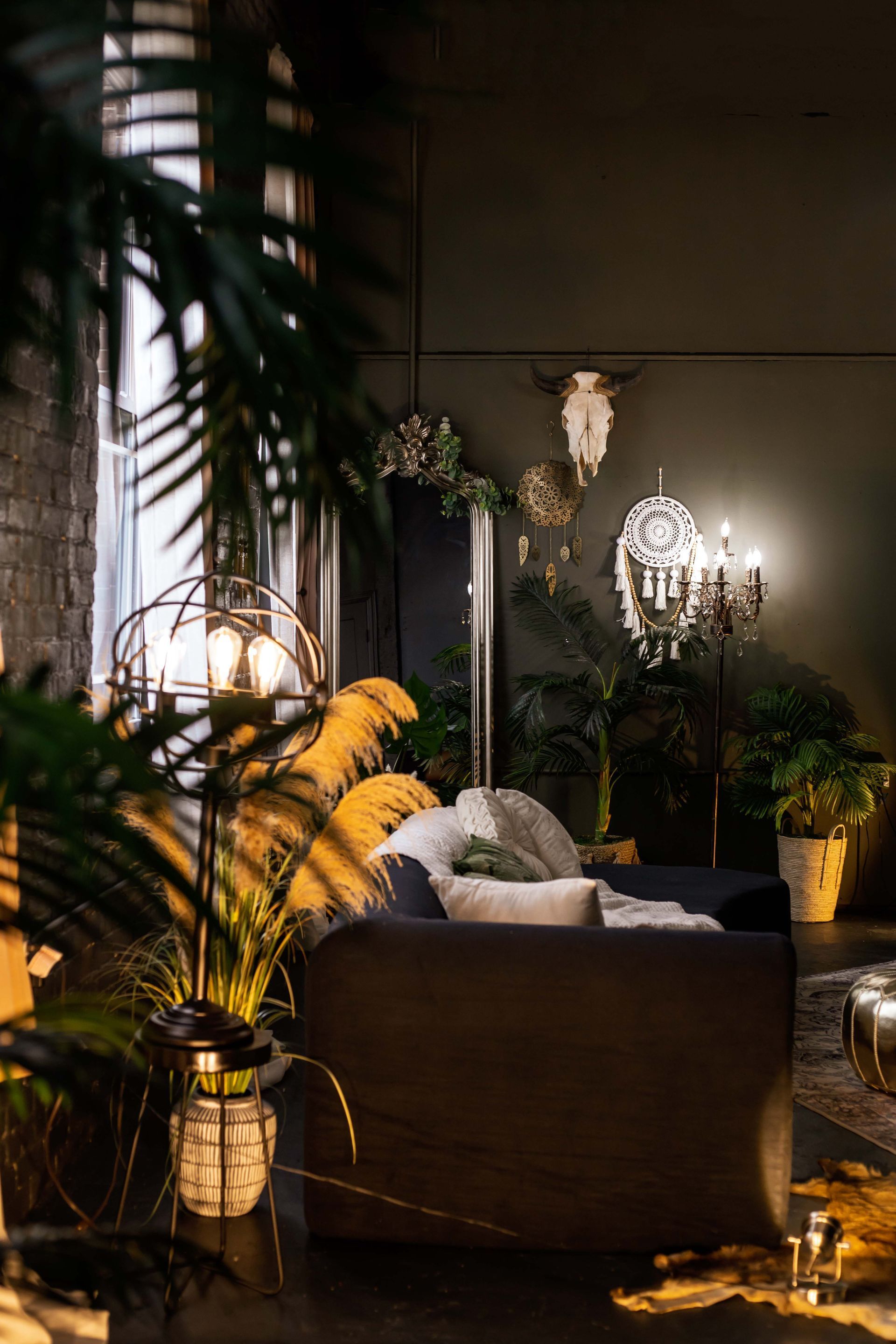 Dim lounge with plush chair, glowing lamps, and lush plants in a dark, stylish interior.