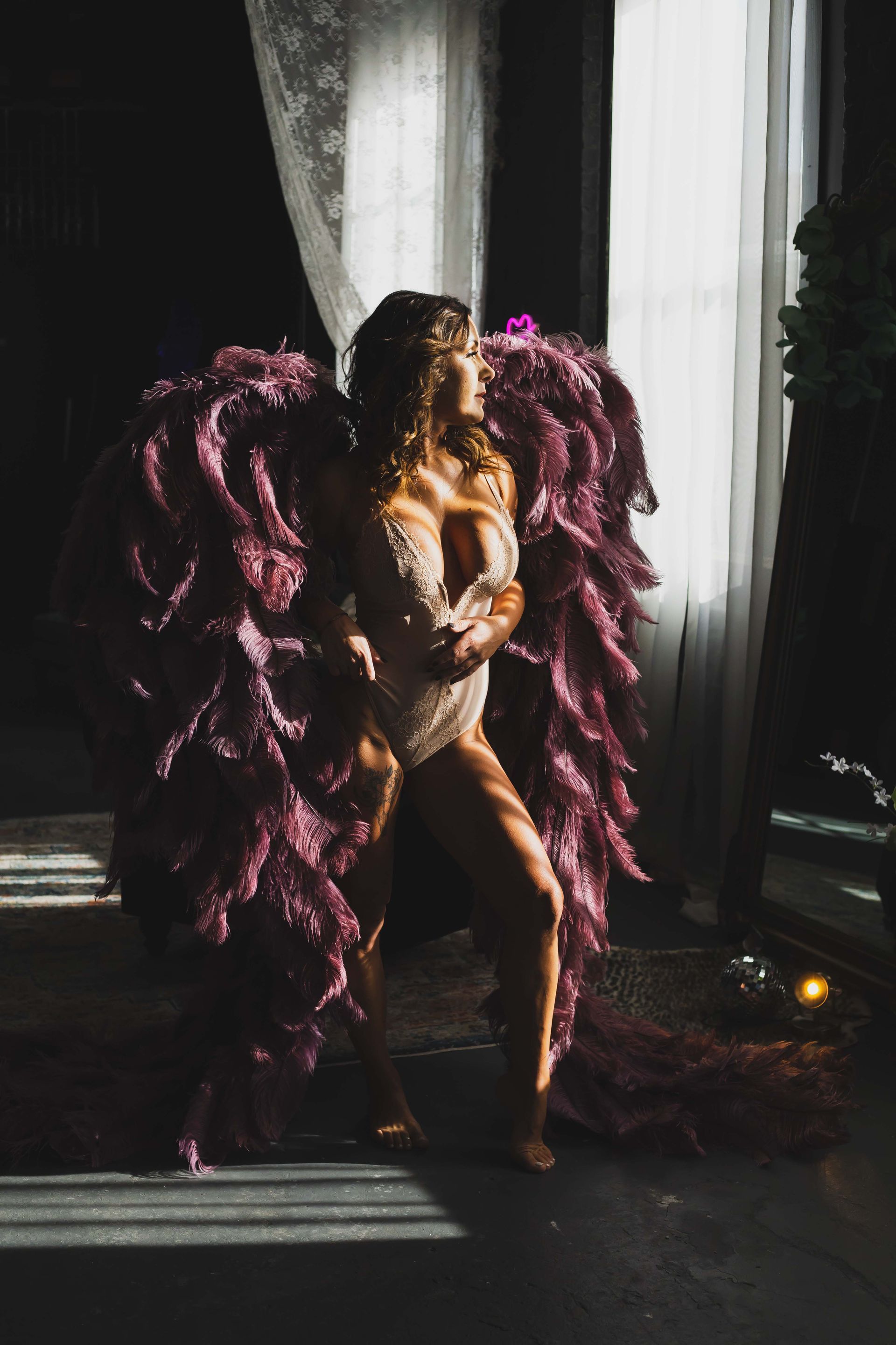 Woman in a white bodysuit and large purple feathered wings, standing in a room with sunlight streaming through a window.