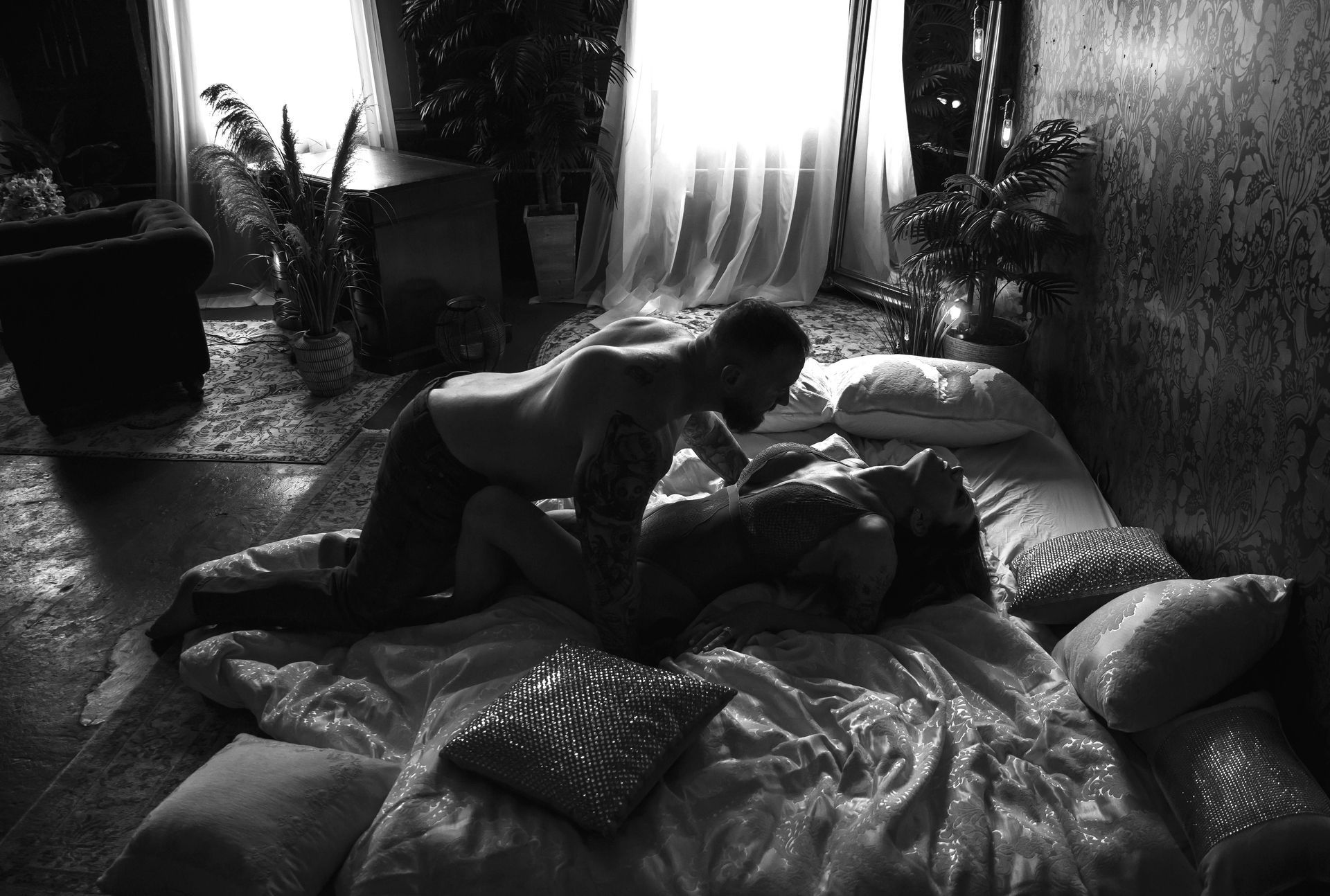 A man leans over a woman on a bed in a dim room. They are engaged in intimate activity.