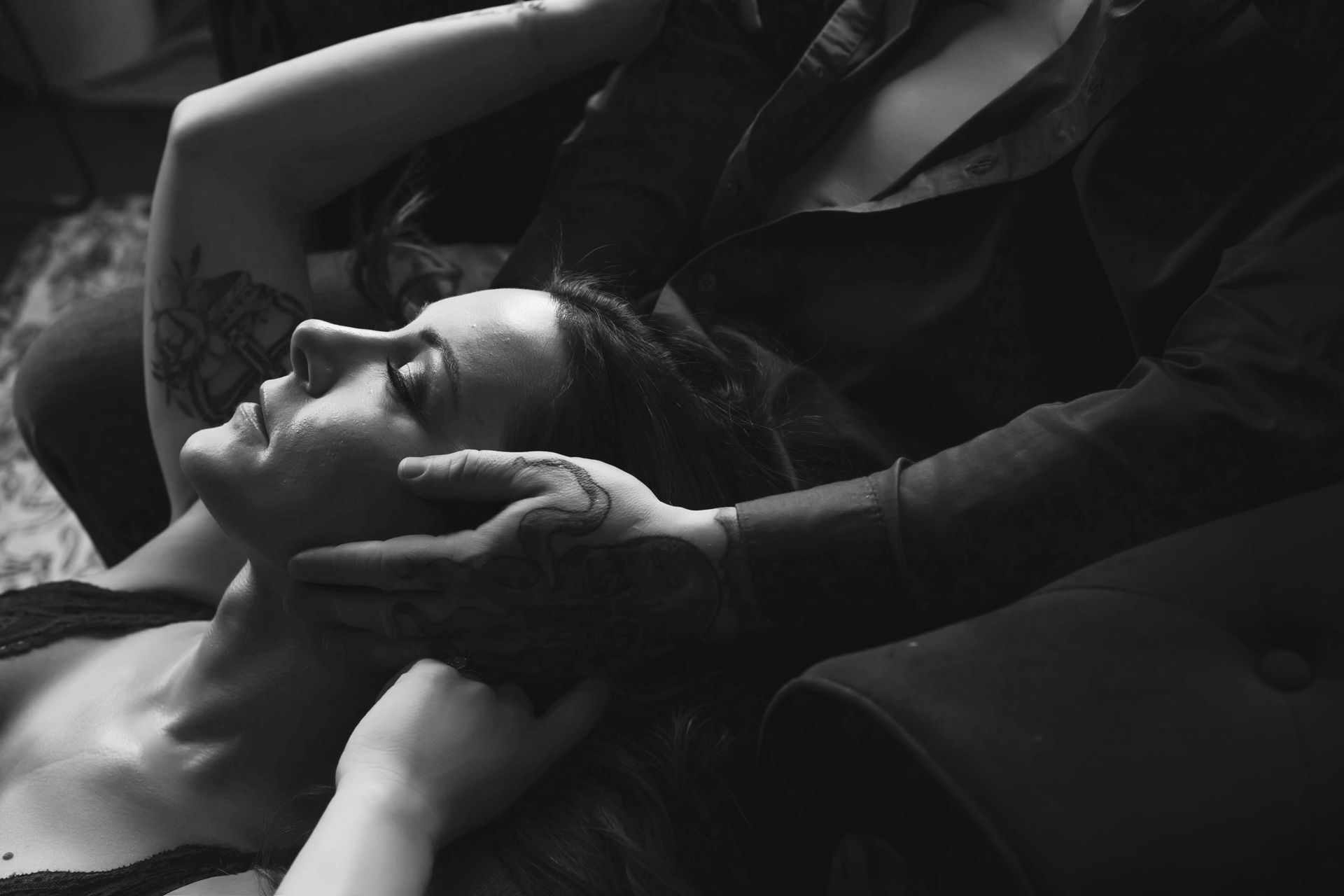 Black and white photo of a person resting with their head tilted back while someone gently cups their face with hands.