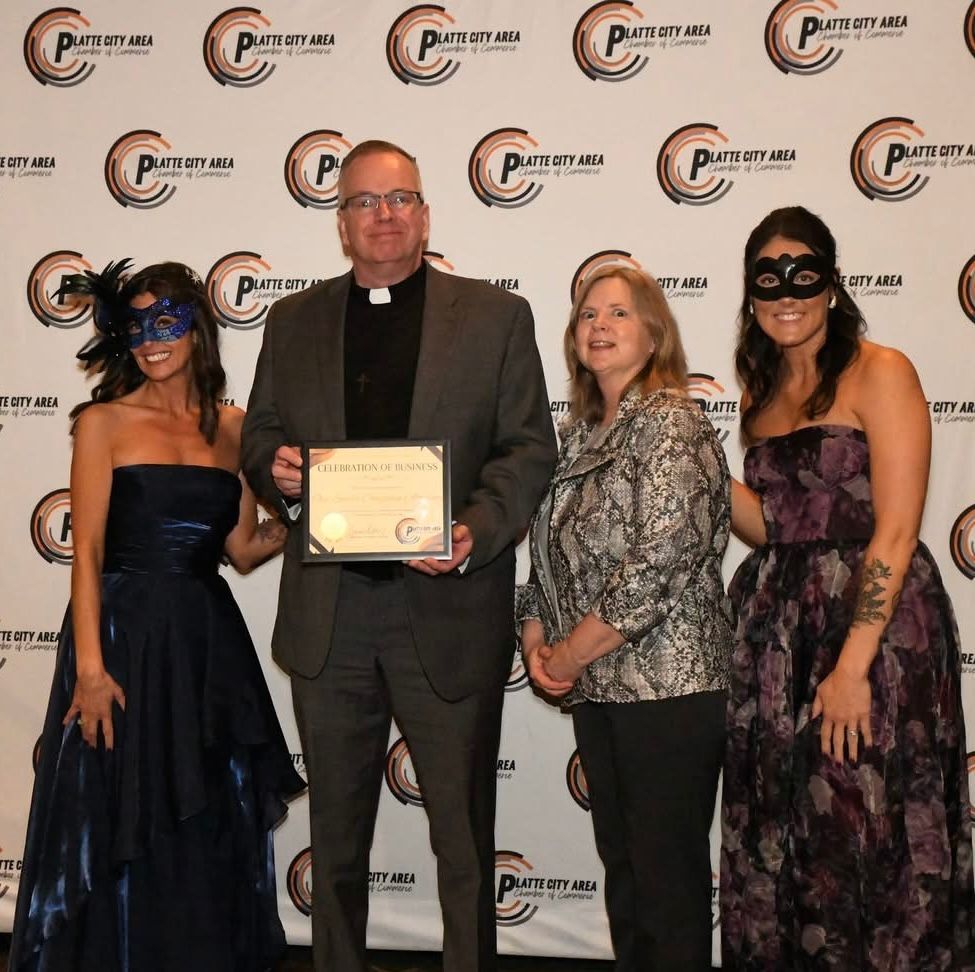 Four people stand for a photo in front of a Plattview Area Chamber of Commerce backdrop; one holds an award plaque.
