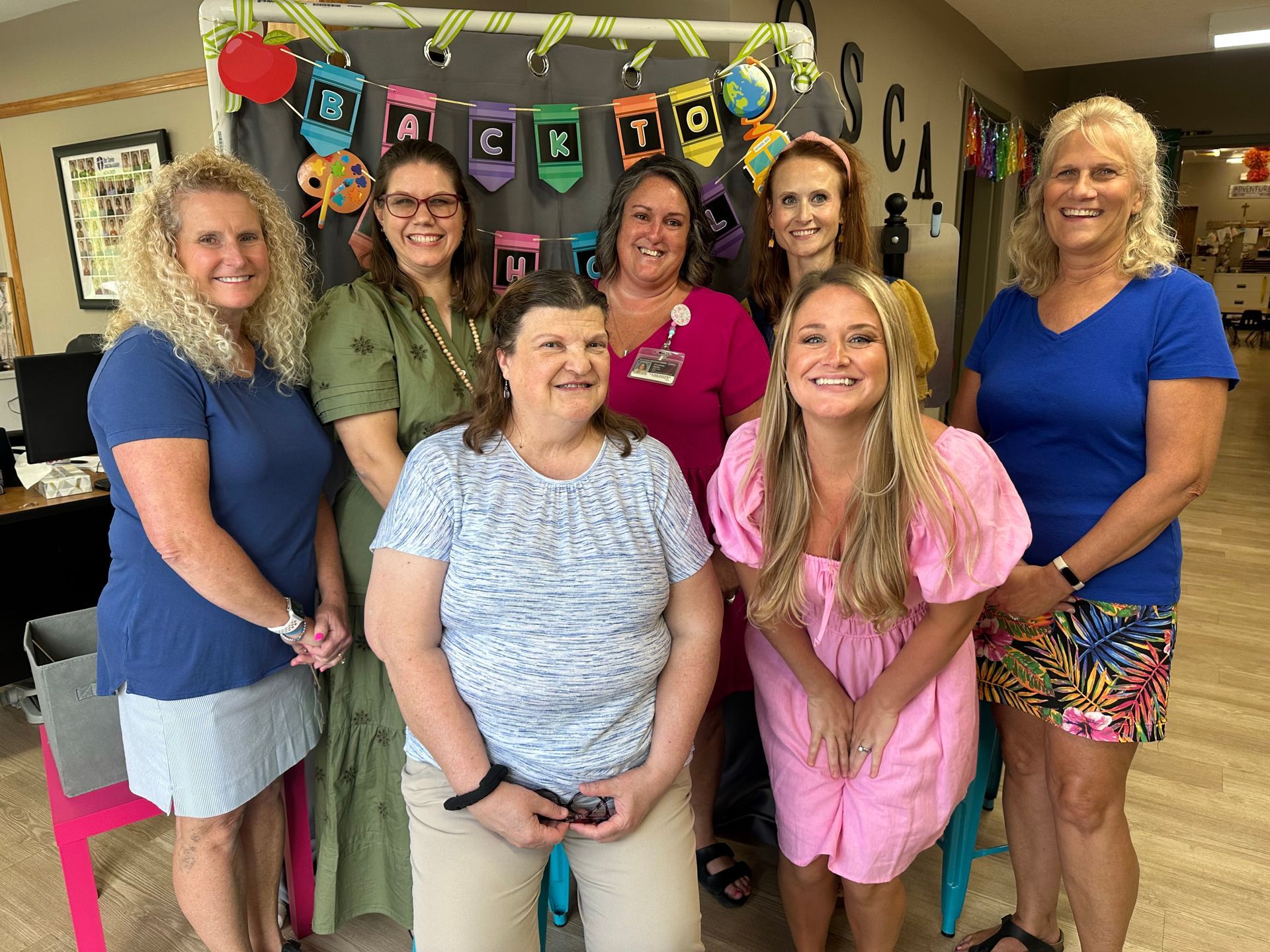 Six people stand smiling in front of a Back to School banner inside a room.
