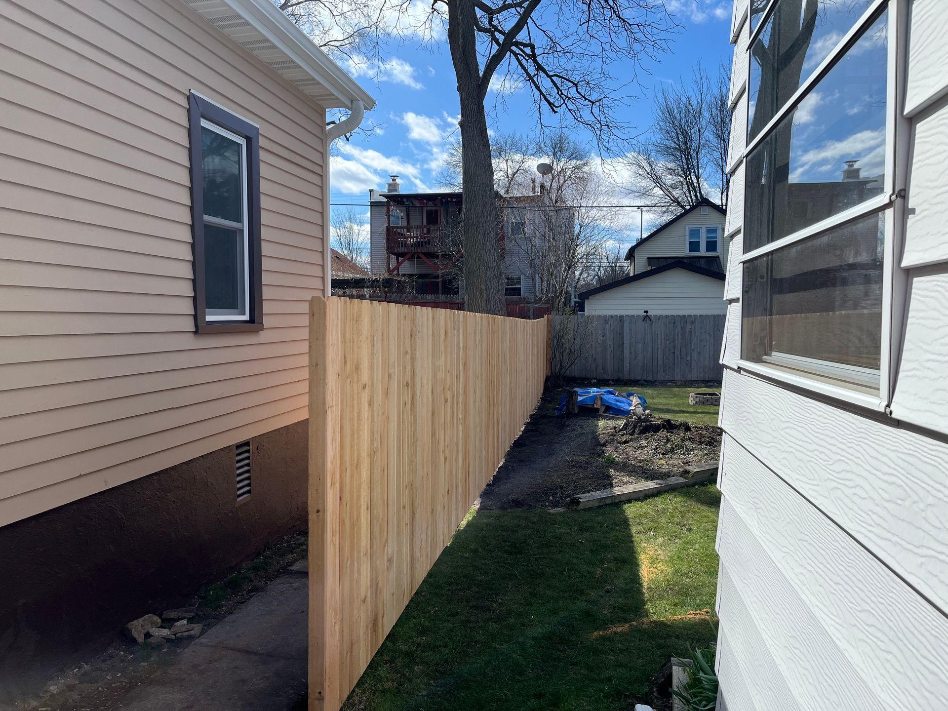 A wooden fence is between two houses in a backyard.