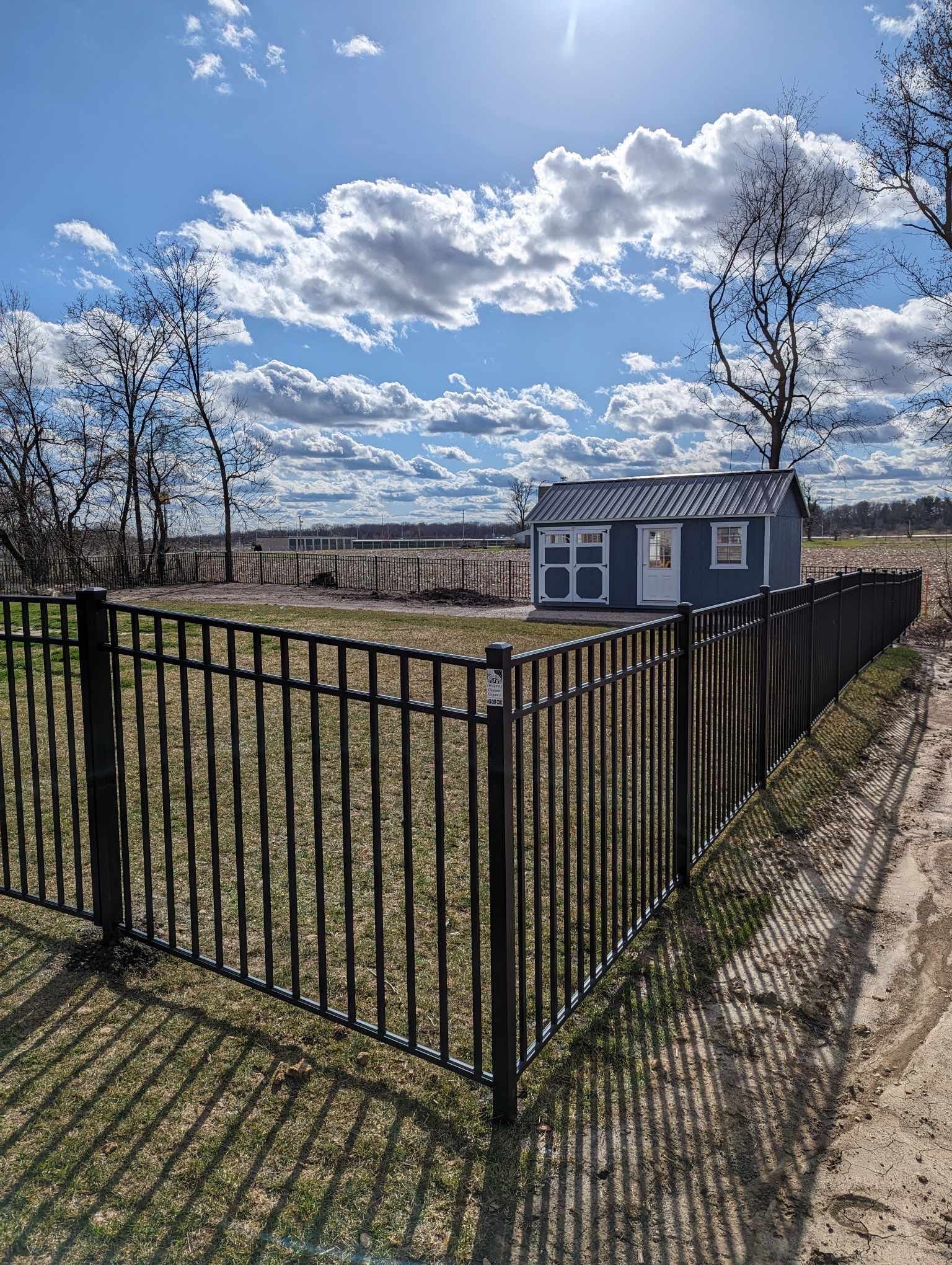 A black fence surrounds a small house in a field.