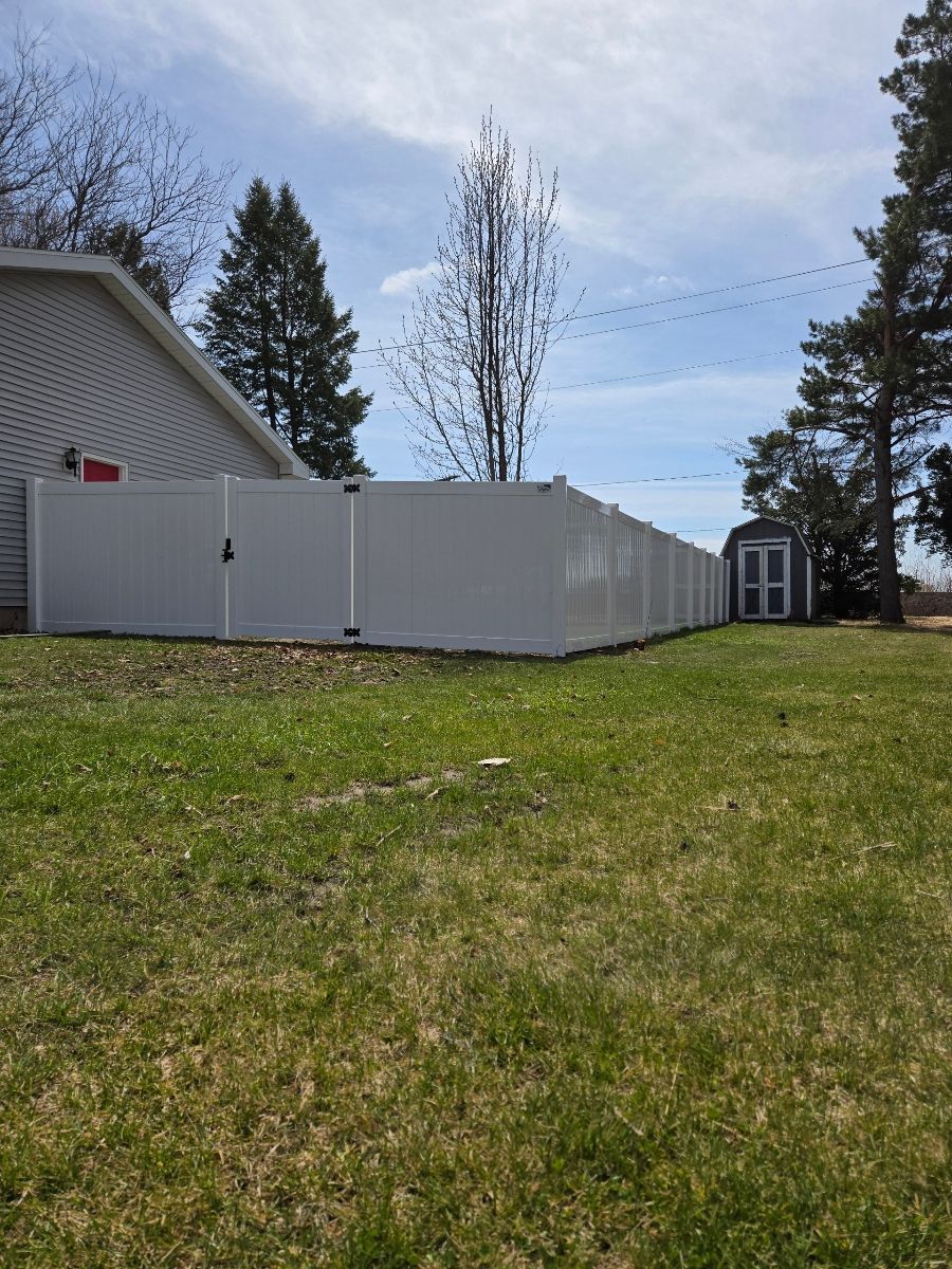 A white fence surrounds a lush green yard in front of a house.