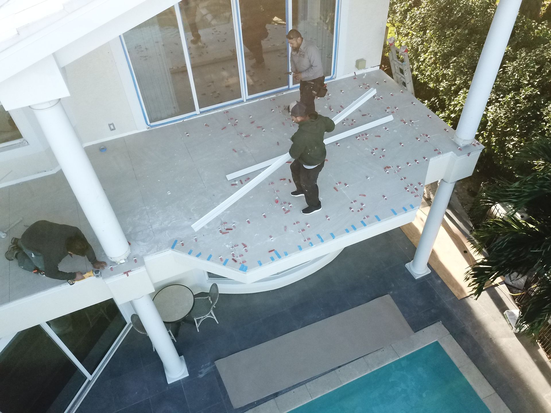 An aerial view of a house under construction with a pool in the background.
