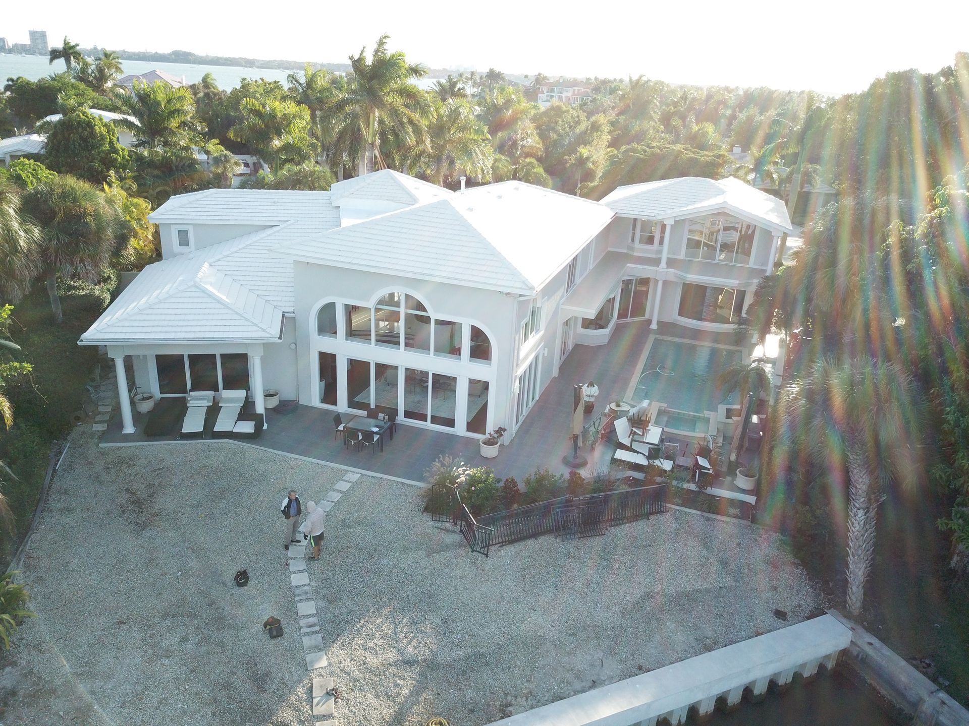 An aerial view of a large white house with a pool surrounded by palm trees.